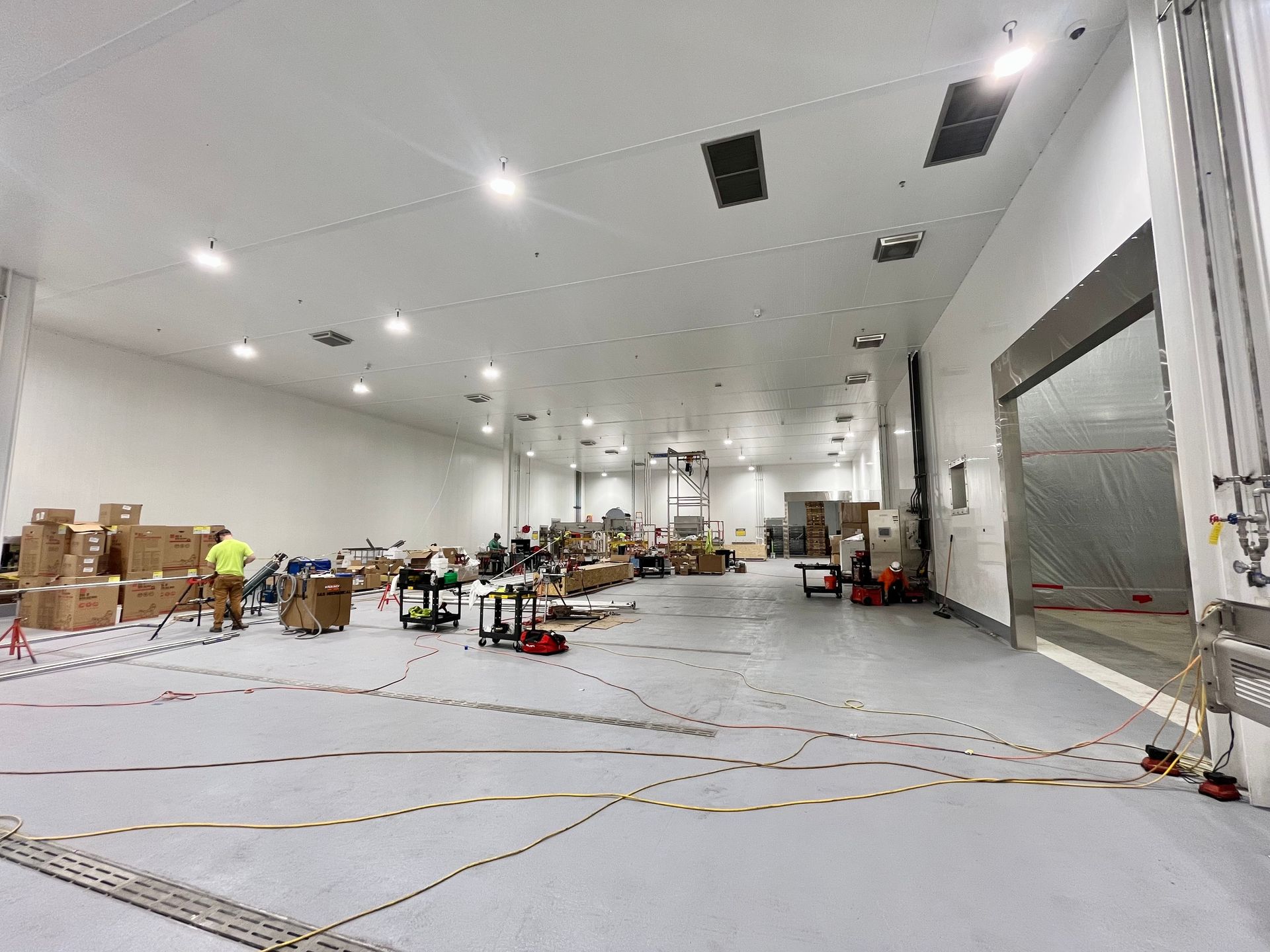 Large, bright warehouse interior with boxes, equipment, and people working. A loading dock is visible on the right side.