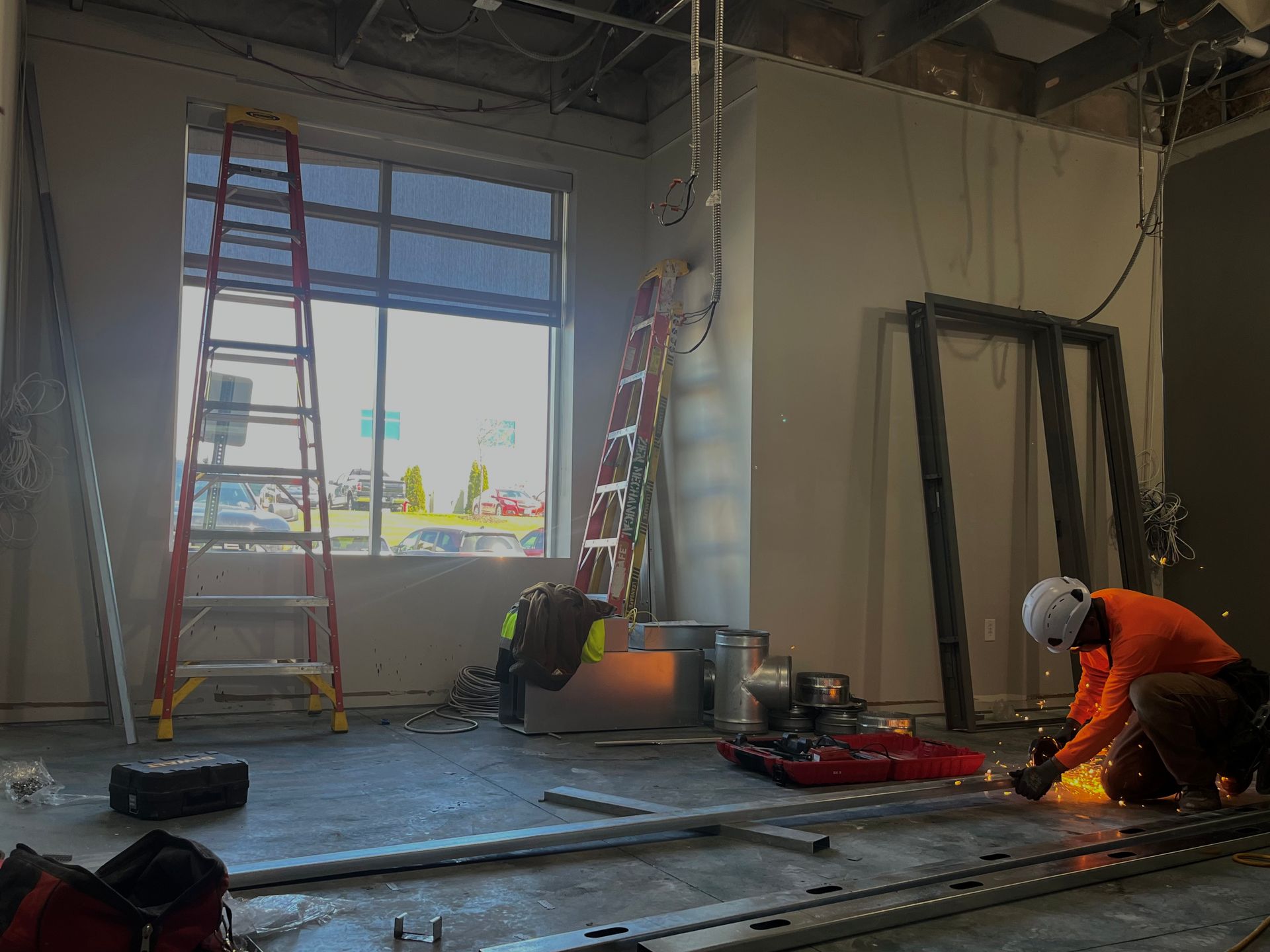 Construction site with workers cutting metal; ladder, window, and tools visible.