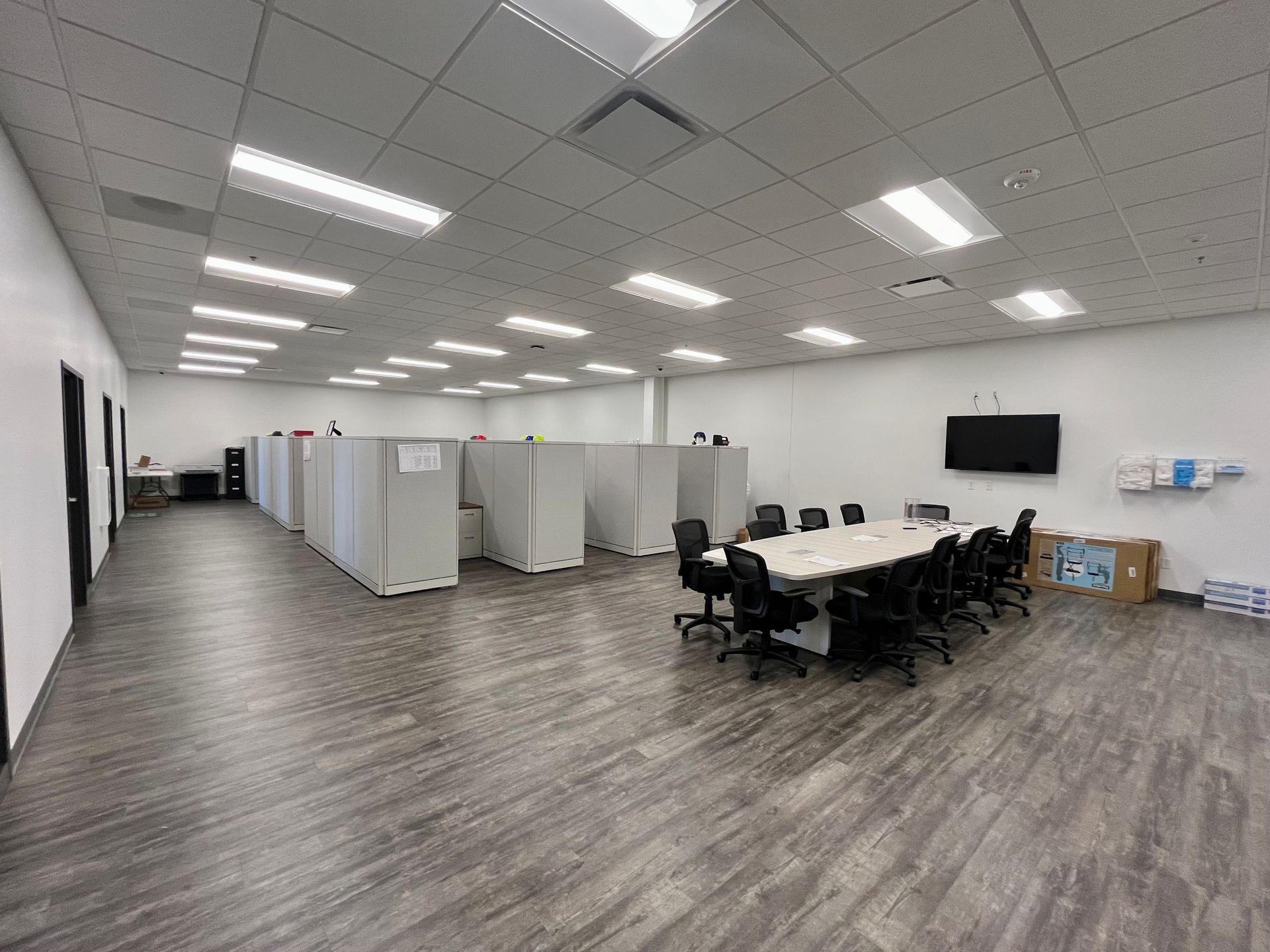 Wide office space with cubicles, conference table, and a mounted TV.