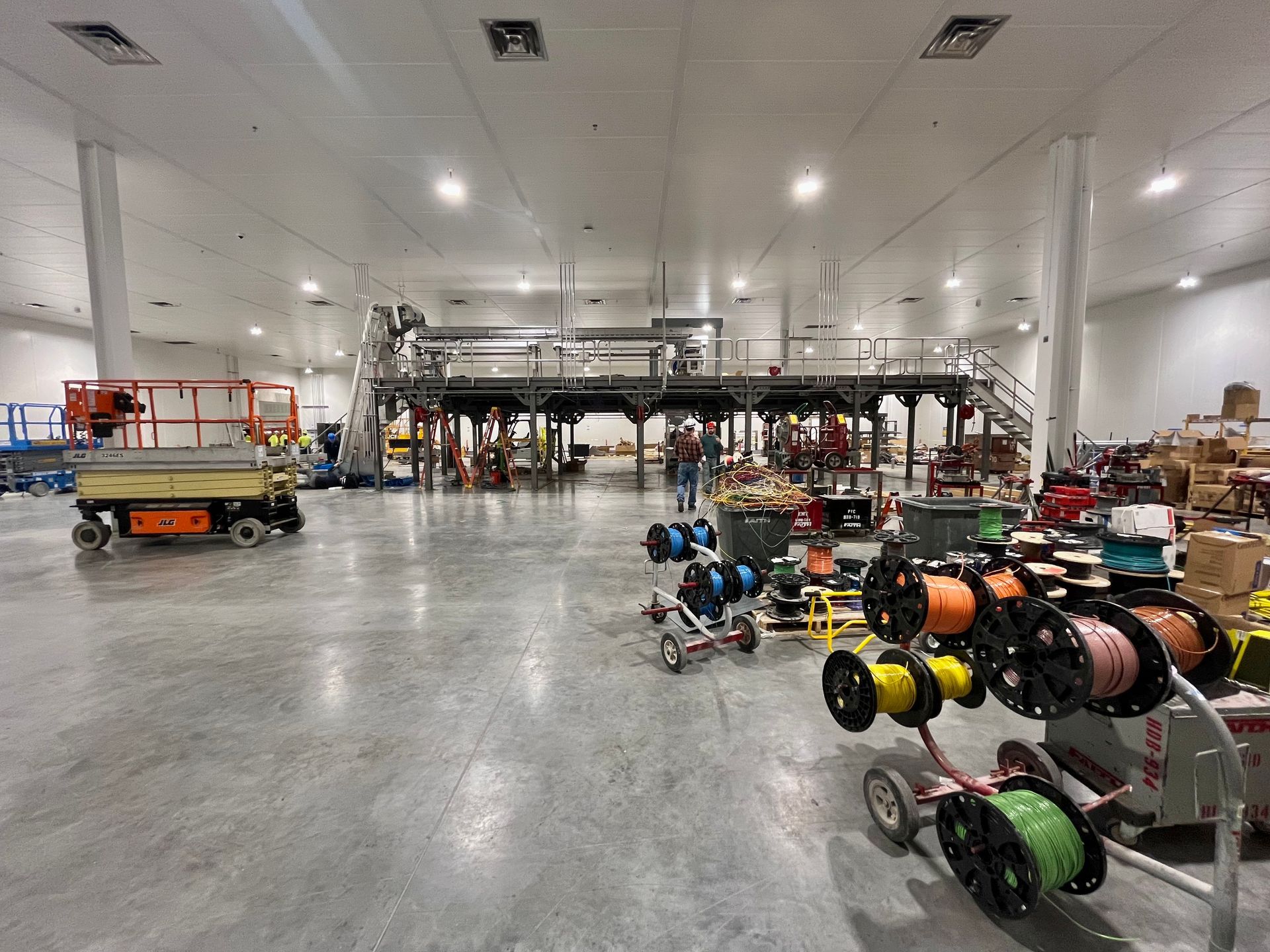 Large industrial space under construction with machinery, wiring spools, and people.