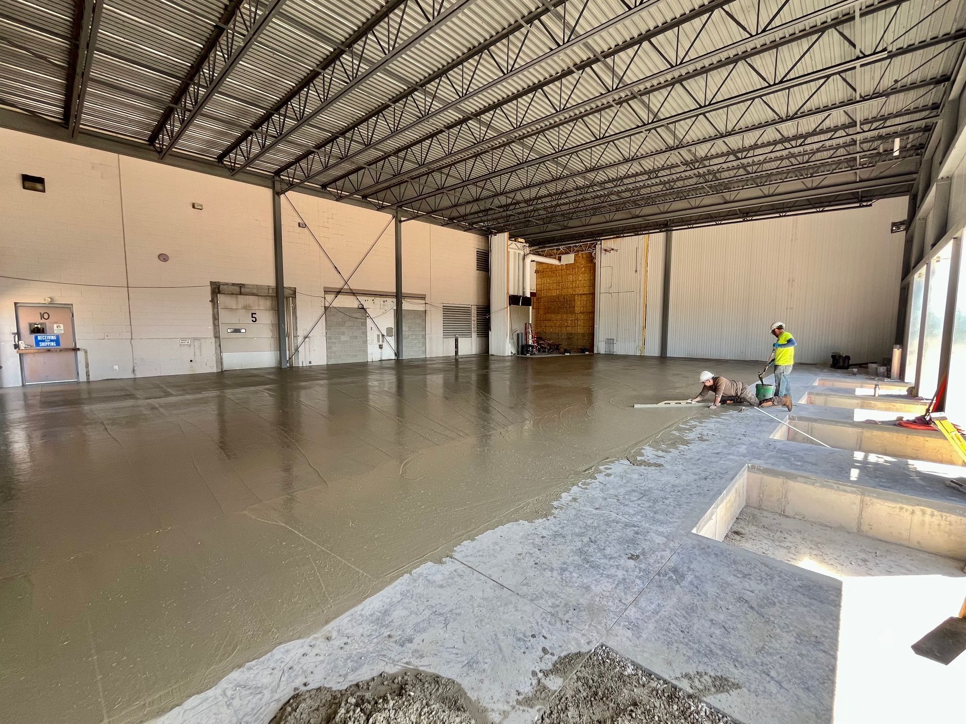 Interior of a commercial building under construction. Concrete floor is being poured. Metal beams support the roof.