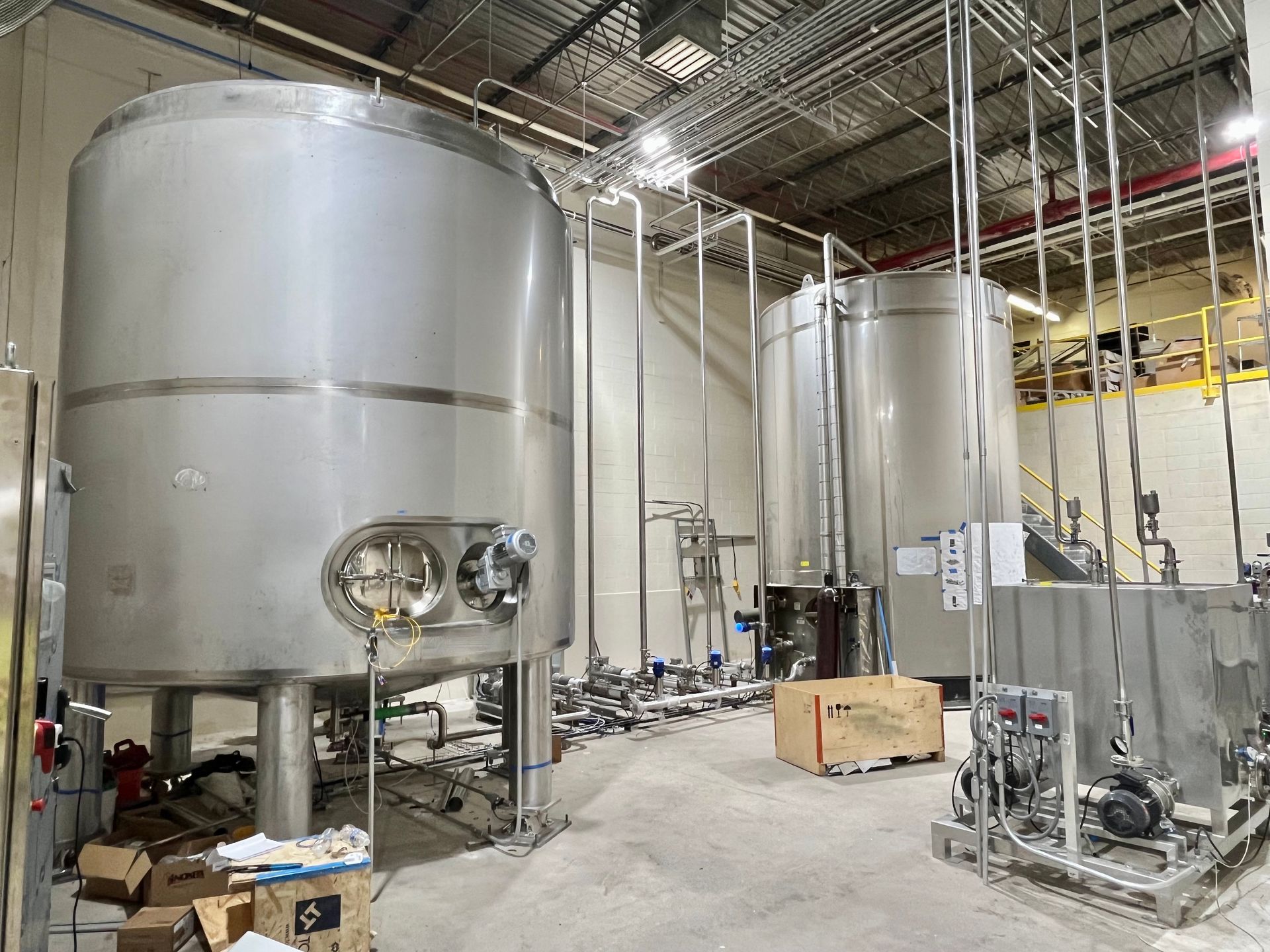 Large stainless steel industrial tanks in a factory setting, with connected pipes and equipment.