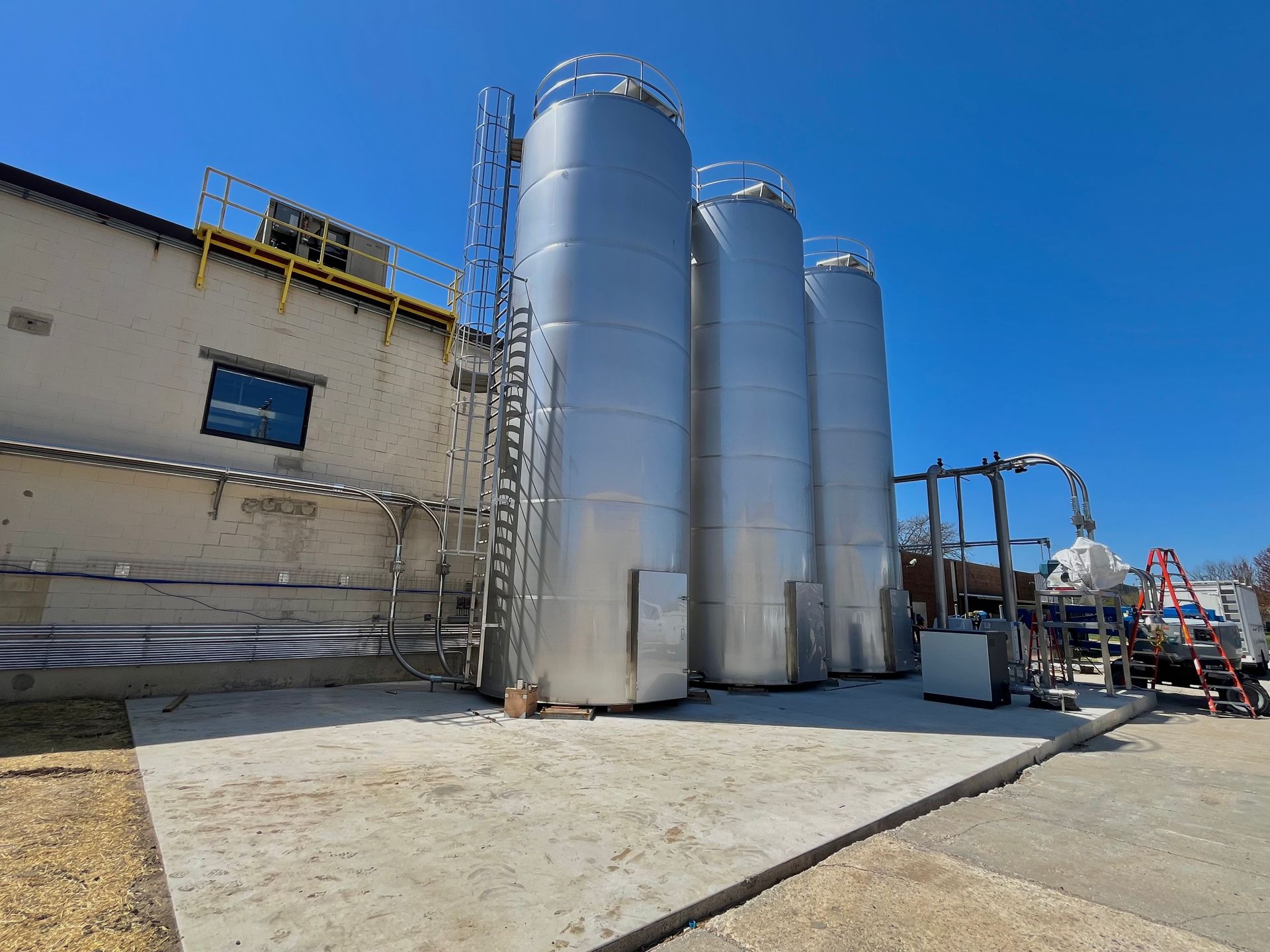 Three silver industrial tanks outside a building on a concrete pad. Clear, sunny day.