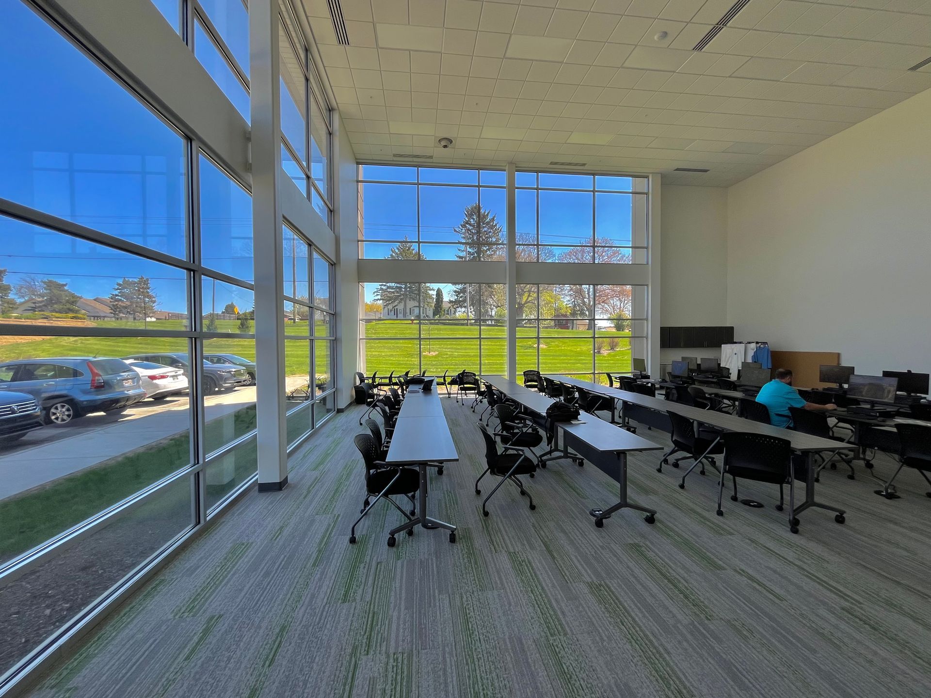 Classroom with large windows overlooking a green lawn. Tables and chairs are arranged for students.