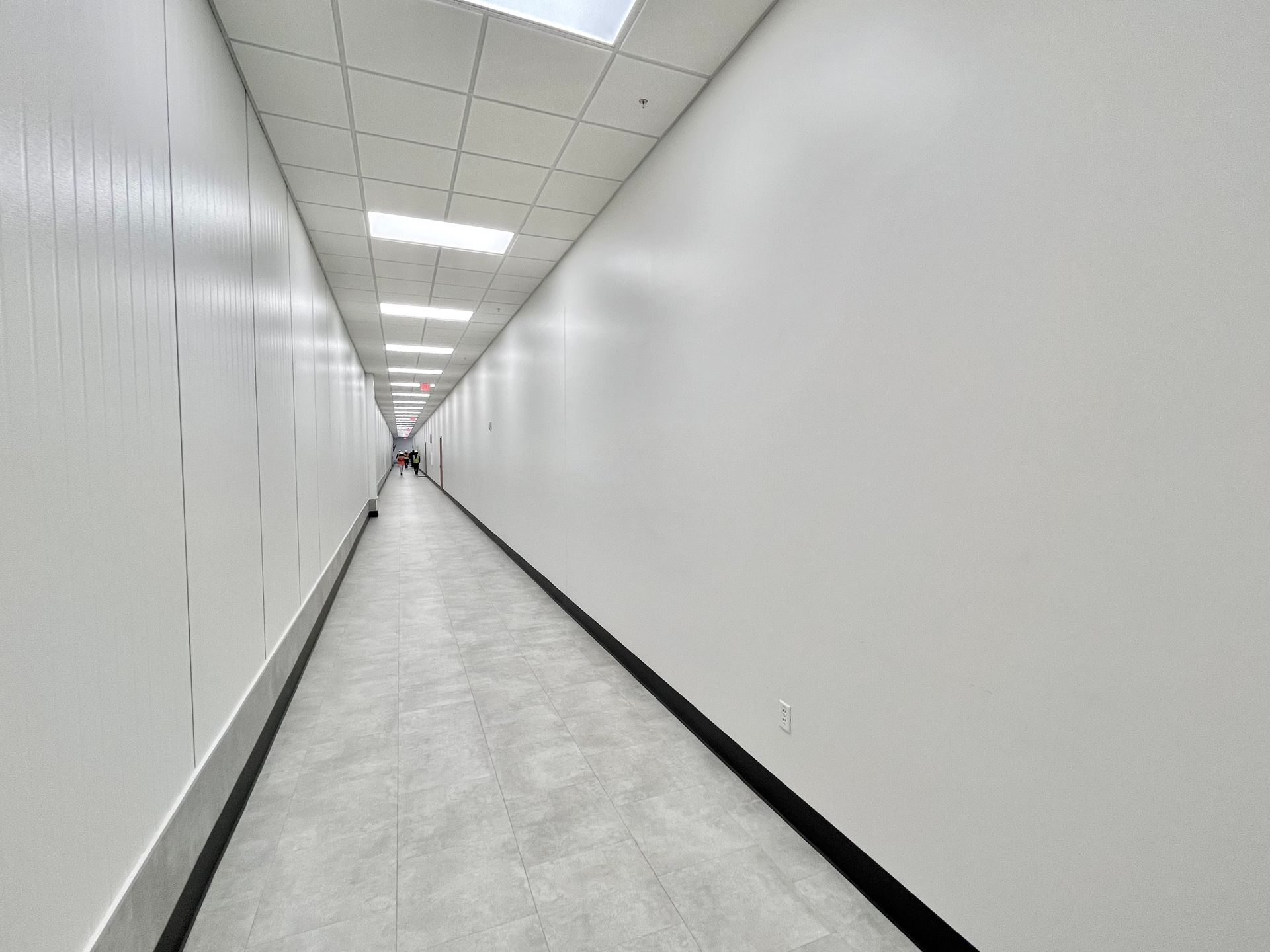 Long, narrow, white hallway with recessed lighting and gray flooring.