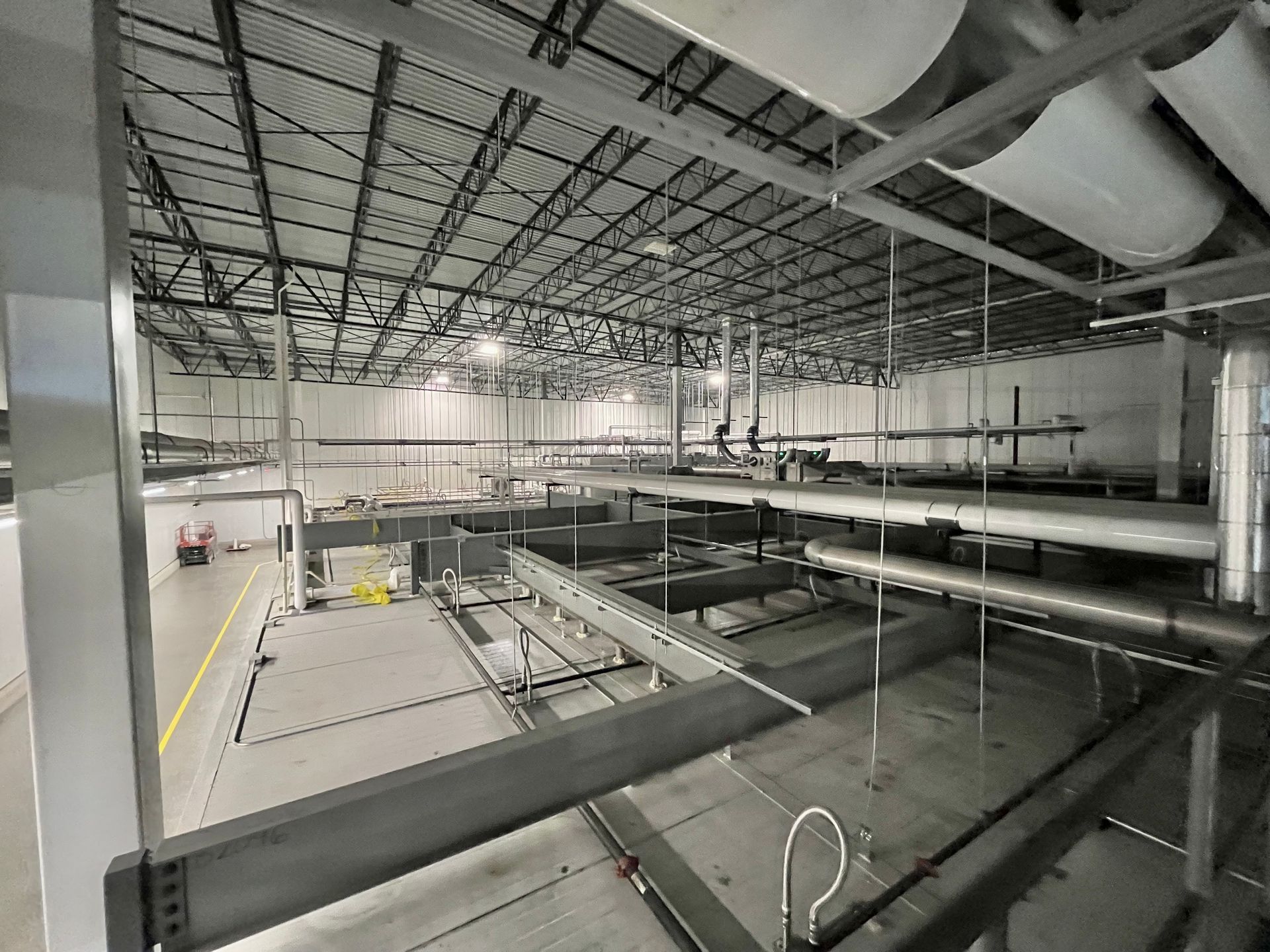 Large industrial interior with exposed metal beams, pipes, and machinery. Gray and white color scheme.