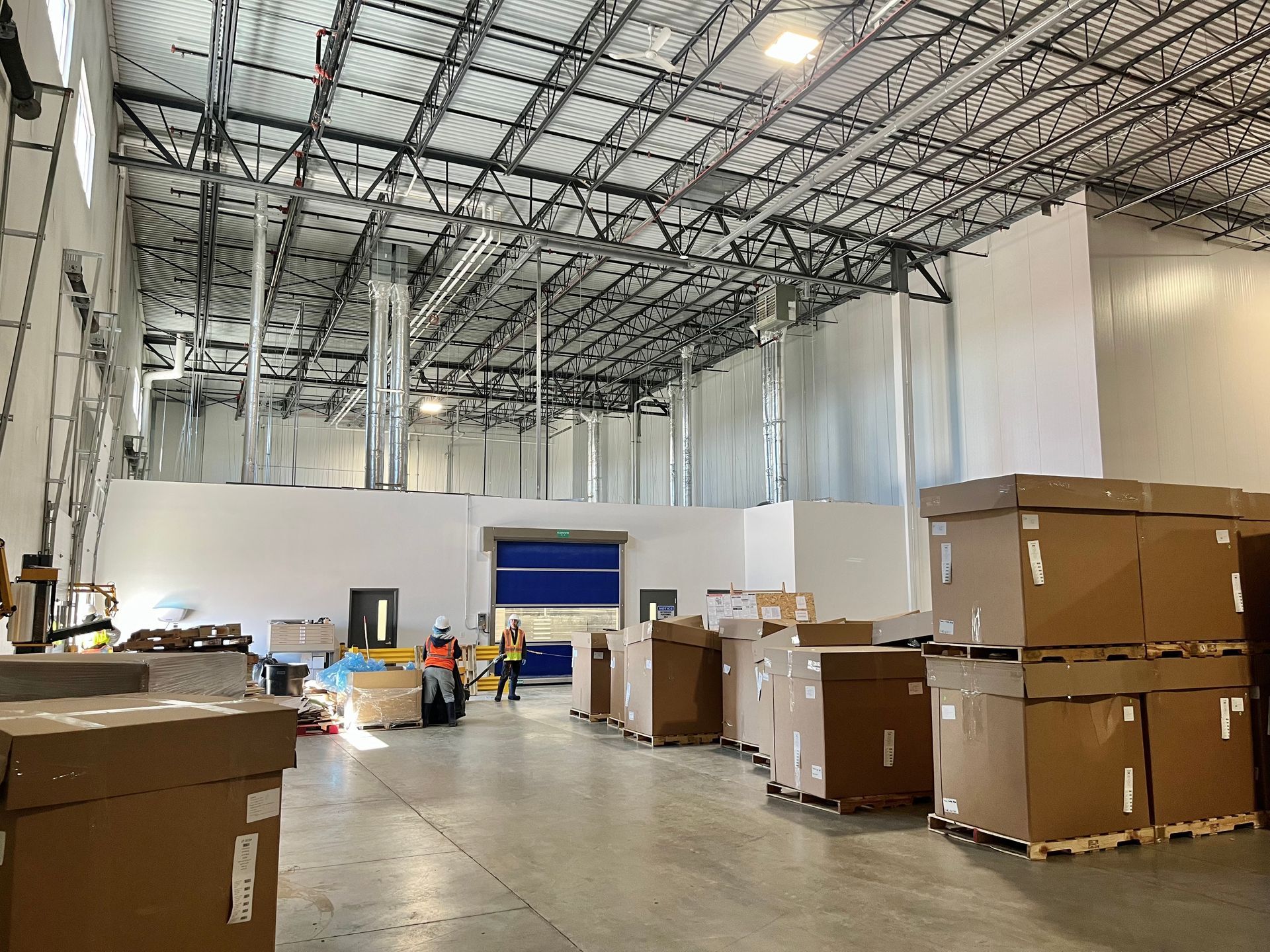 Warehouse interior with cardboard boxes, a blue door, and workers.