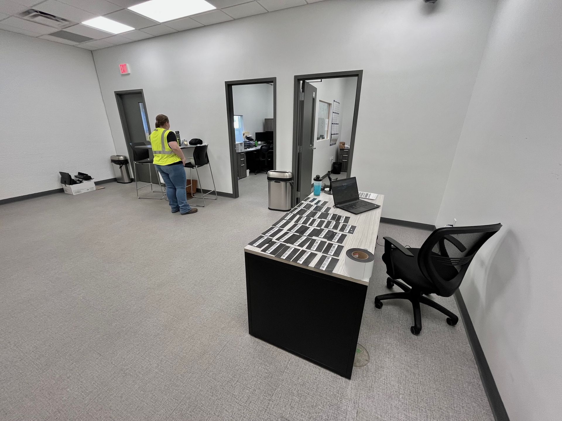 Office interior with desk, person working, two open doorways, and gray carpet.