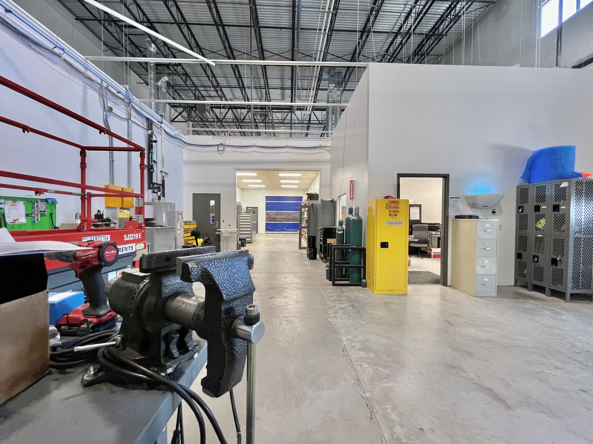 Workshop interior with a vise in foreground, machinery, and white walls.