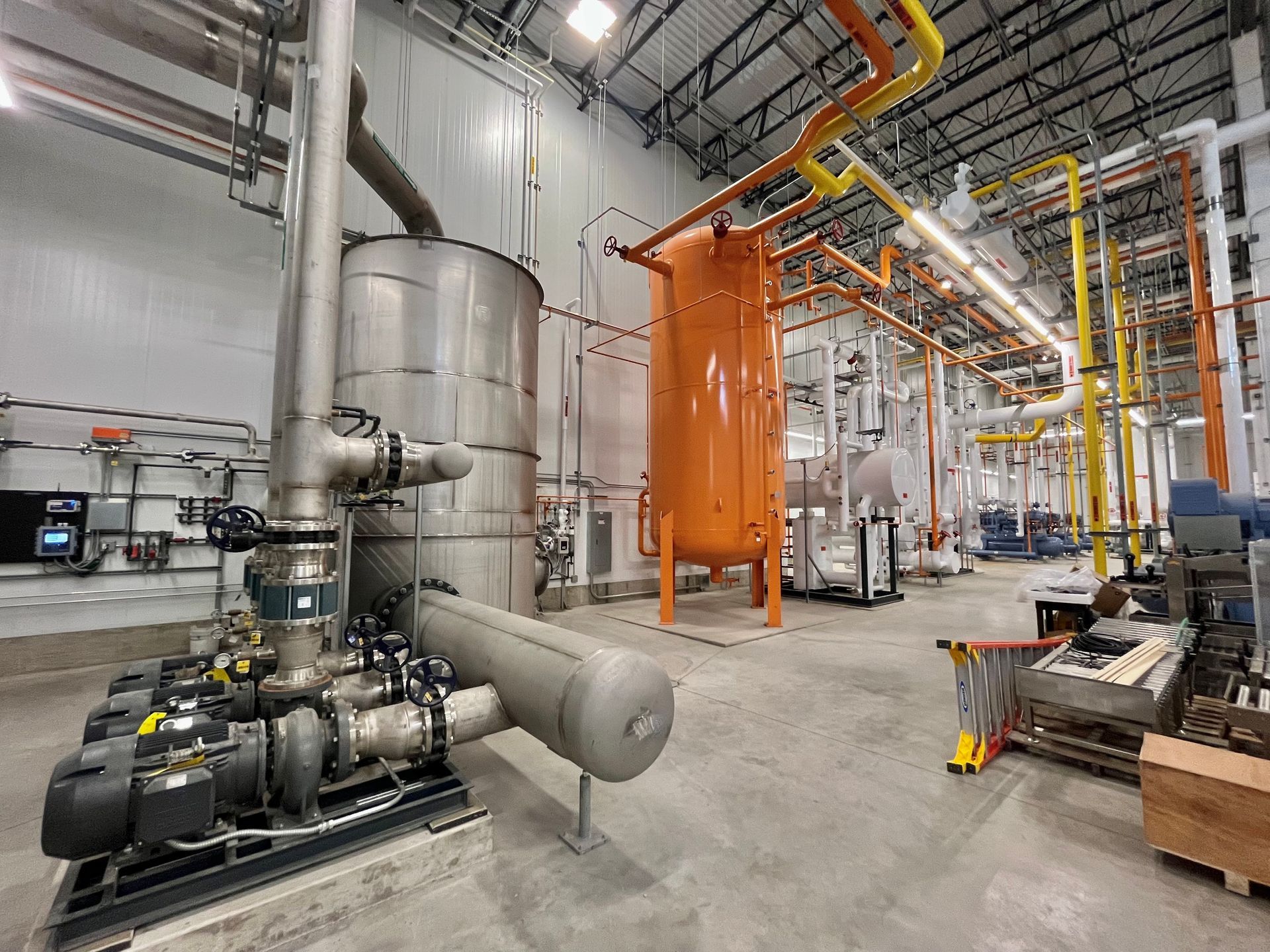 Industrial facility interior with large tanks, piping, and machinery.