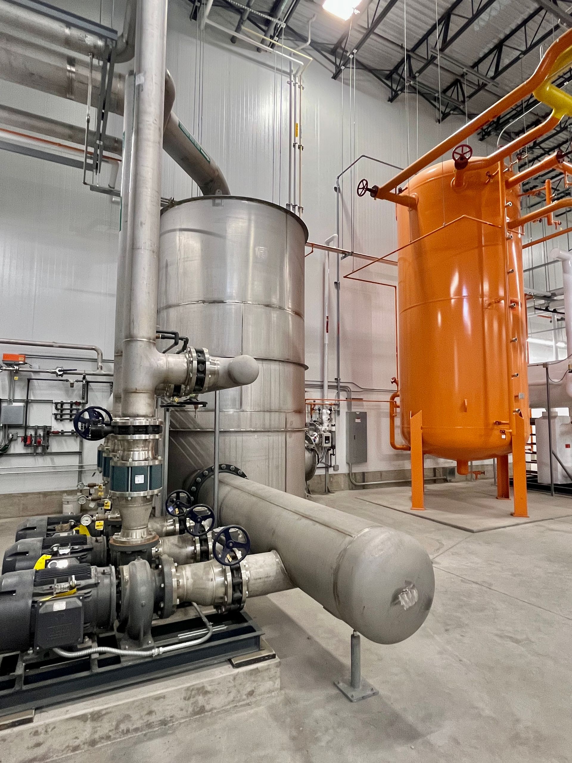 Industrial equipment in a clean room setting, including a silver tank, orange tank, and pipes.