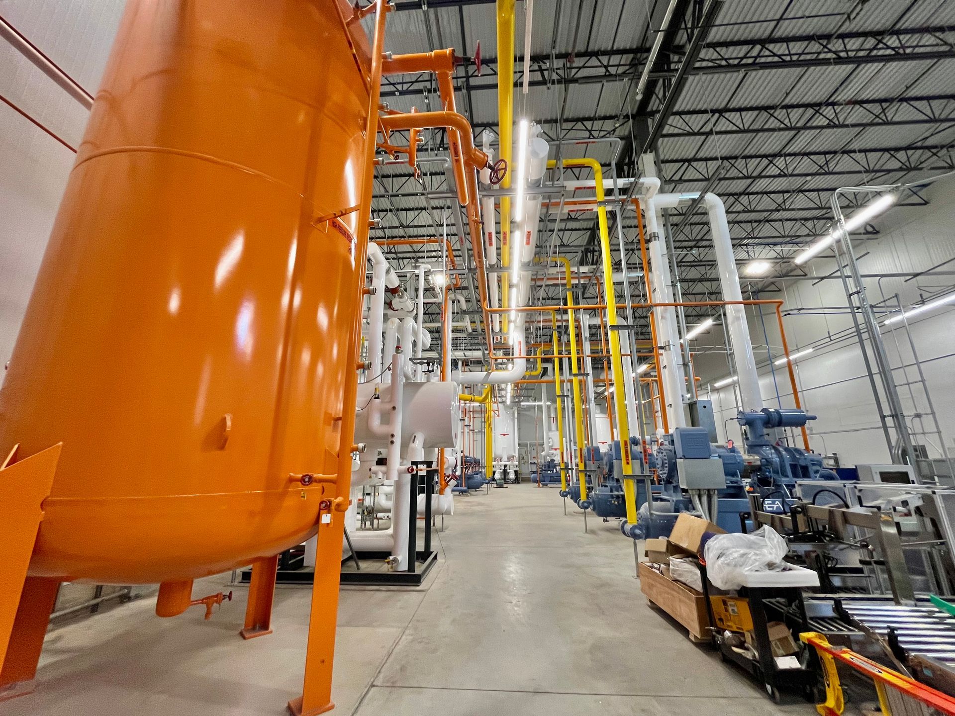 Orange industrial tank and complex pipes in a brightly lit facility.