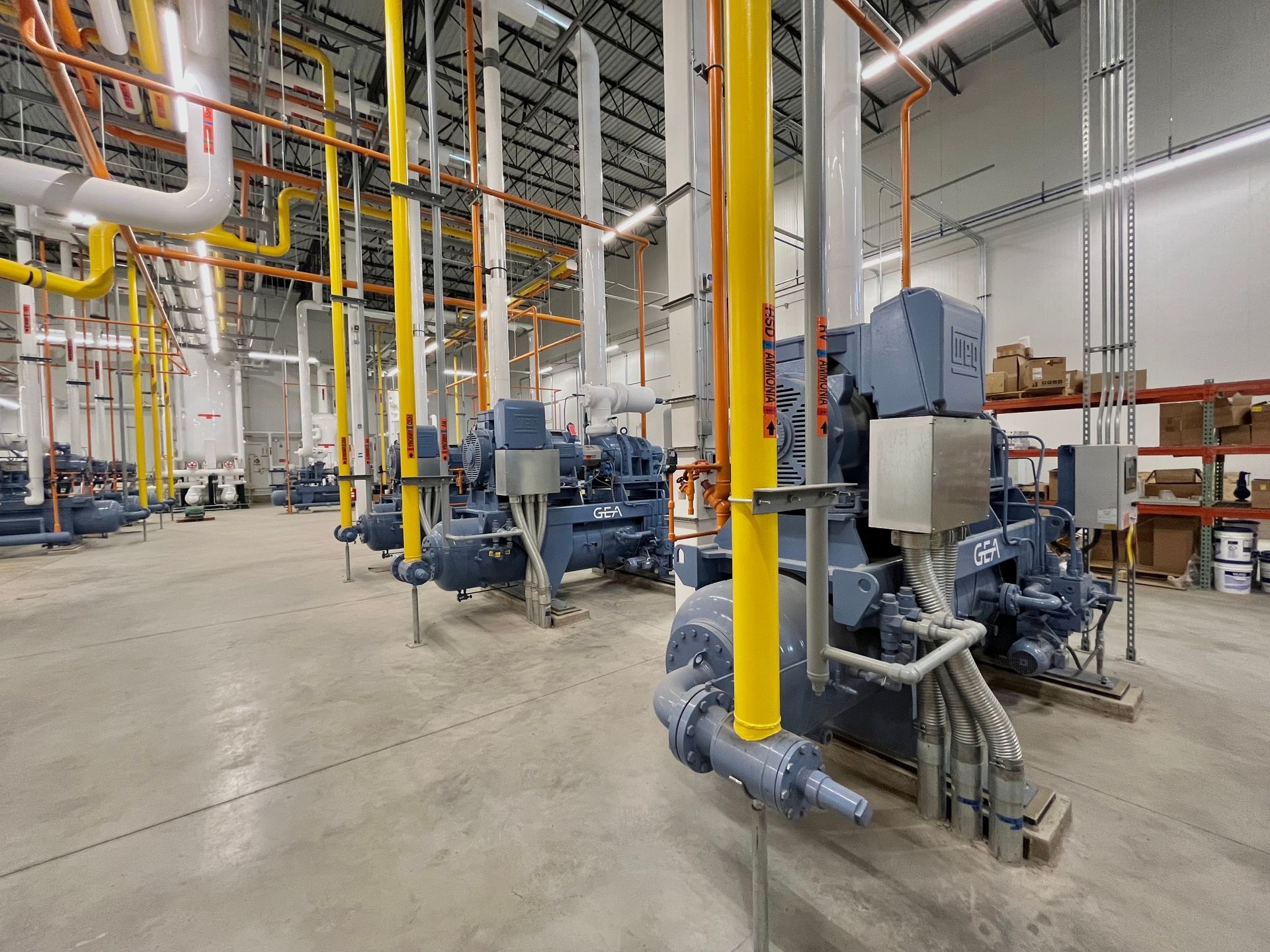 Large industrial refrigeration units in a warehouse setting, with yellow and white pipes overhead.