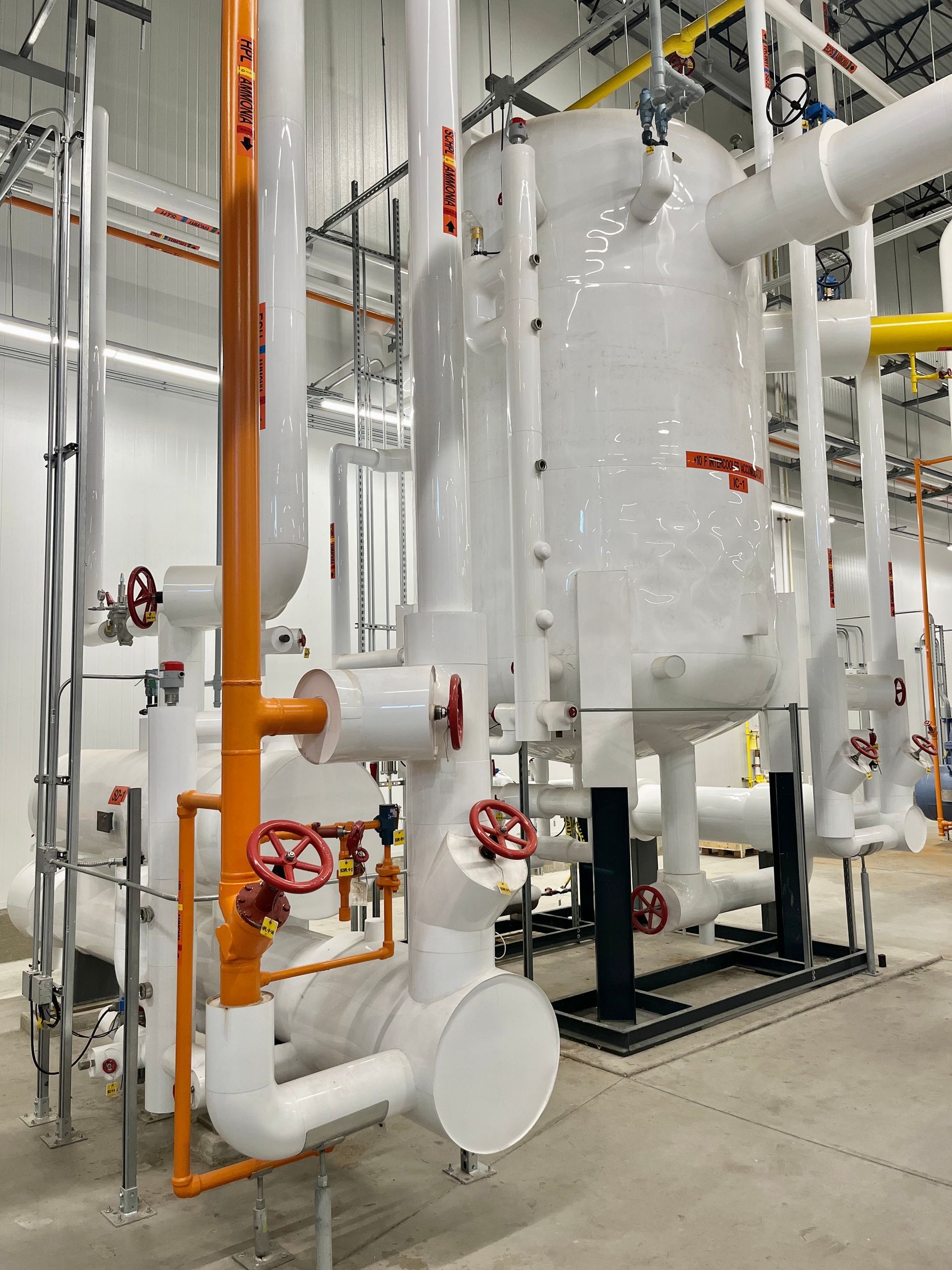 Industrial pipes and tanks, insulated with white and orange coverings, in a commercial building.