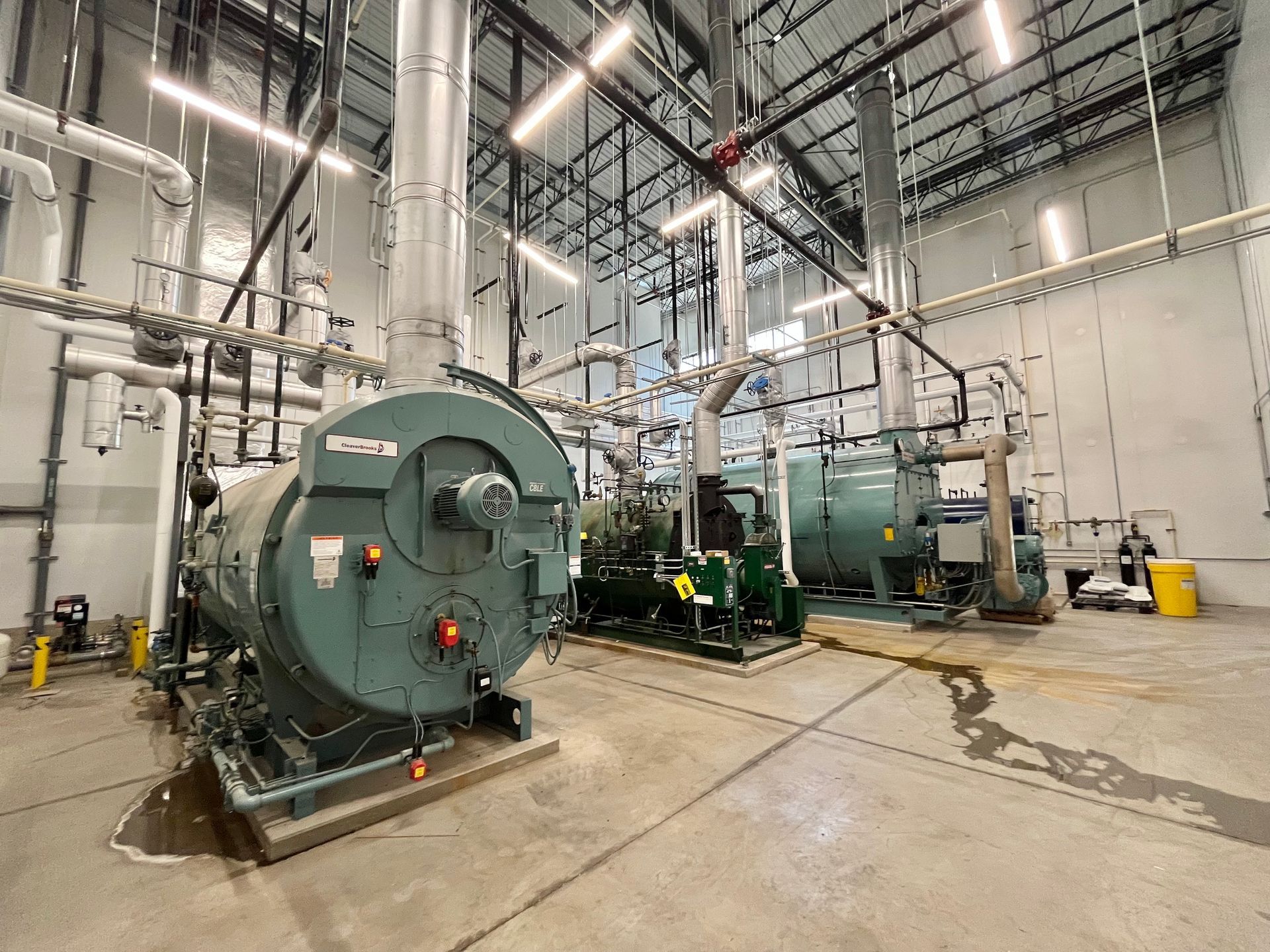 Industrial equipment in a mechanical room with pipes, tanks, and machinery; gray and green hues.