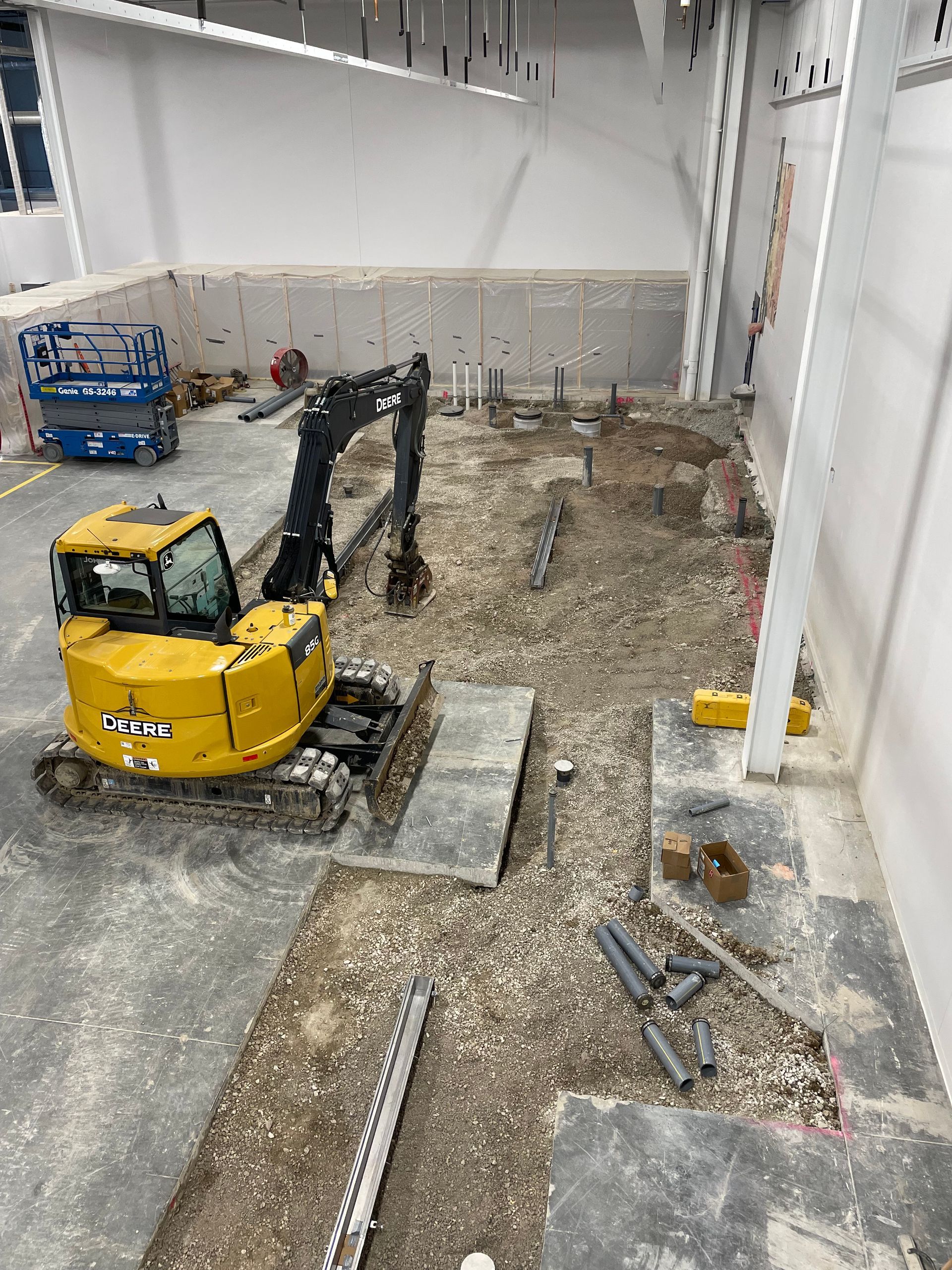 Yellow excavator working inside a building under construction, tearing up concrete floor.