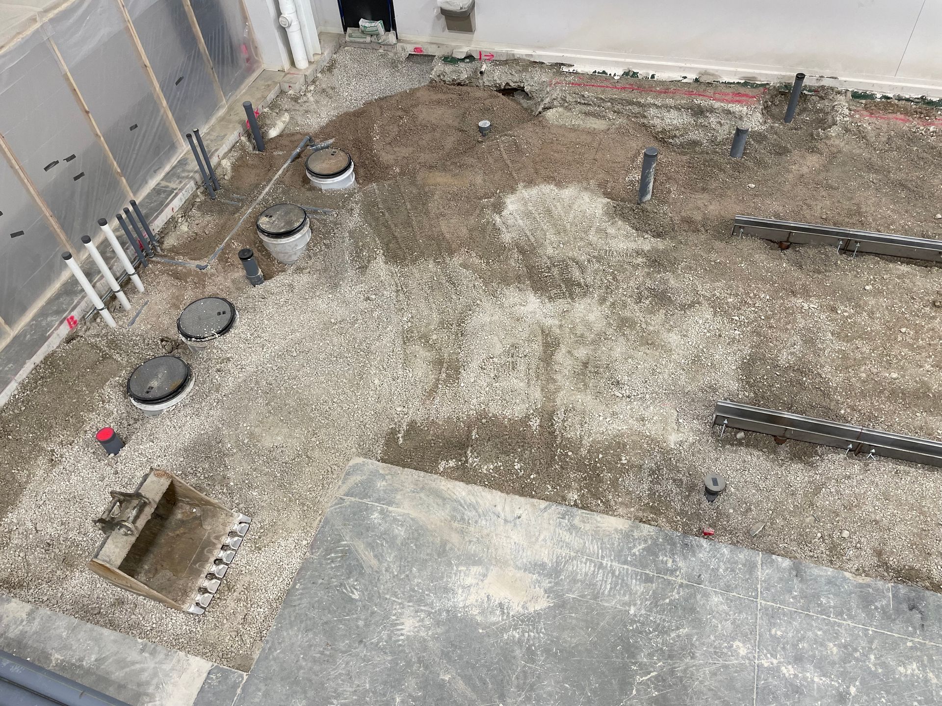 Overhead view of a construction site with gravel, pipes, and manhole covers.