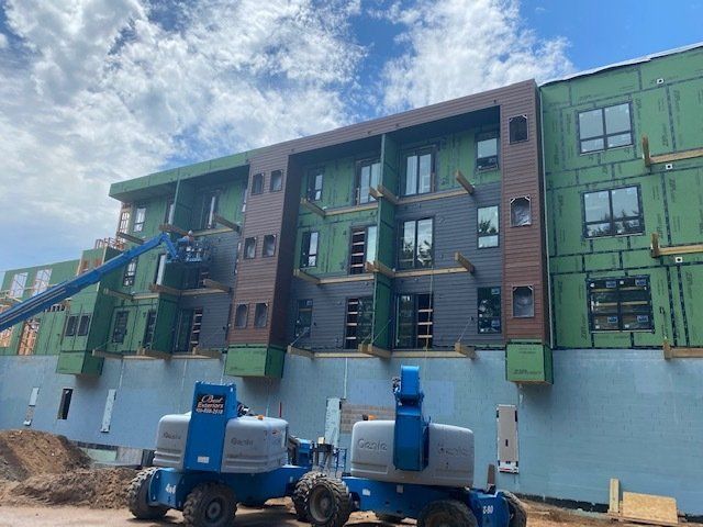 Multi-story building under construction with blue lift machinery and partially installed siding.