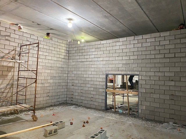 Interior construction site with gray cinder block walls, partially built room, scaffolding, and workers.