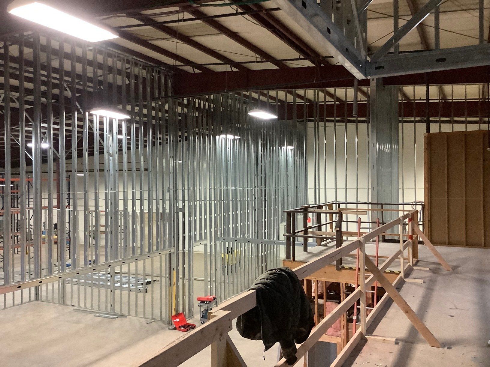 Interior view of a building under construction. Metal studs line walls, with a wooden railing and beams overhead.