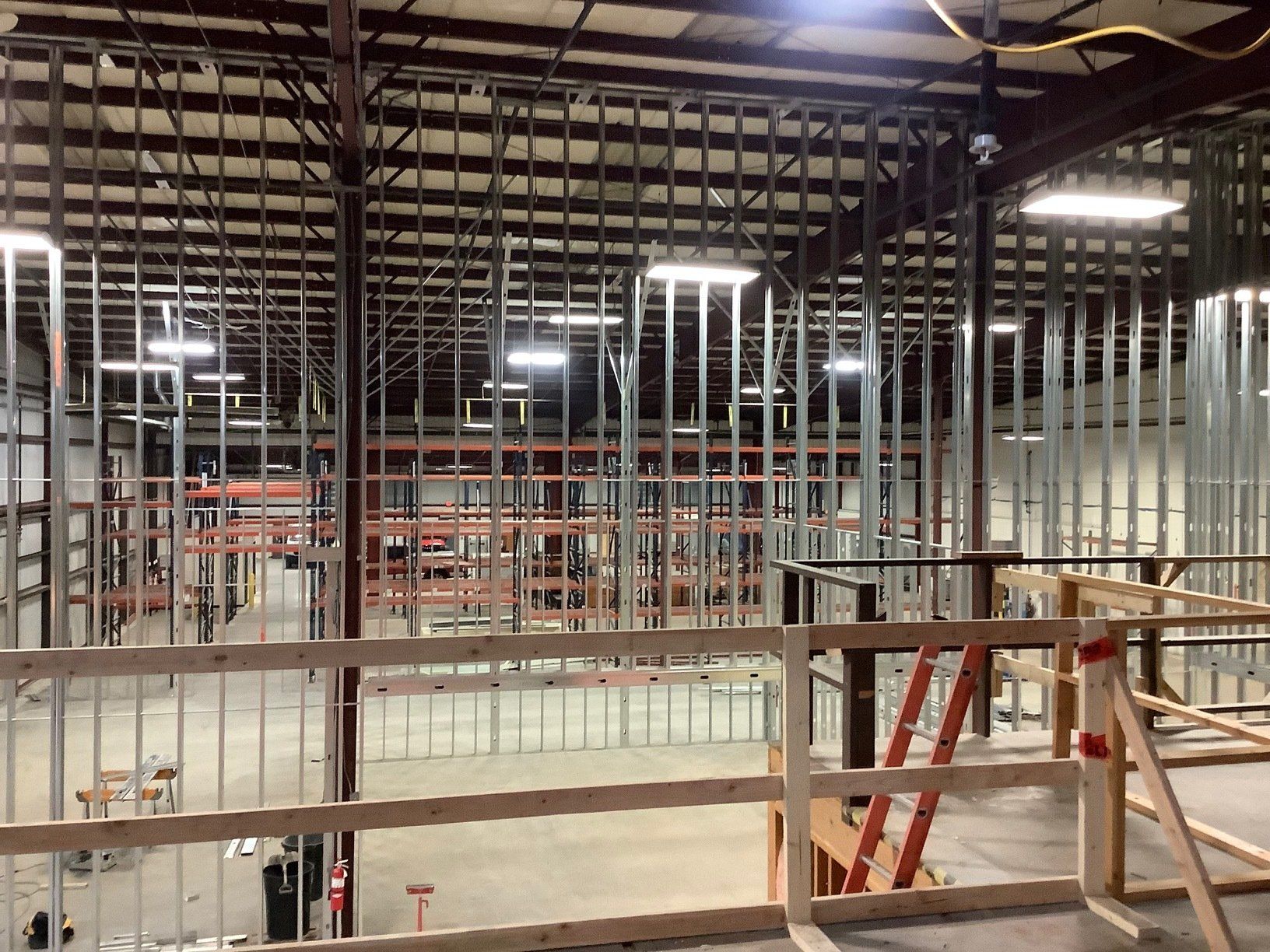 Interior view of a warehouse under construction, with metal framing and a partially built wooden balcony.