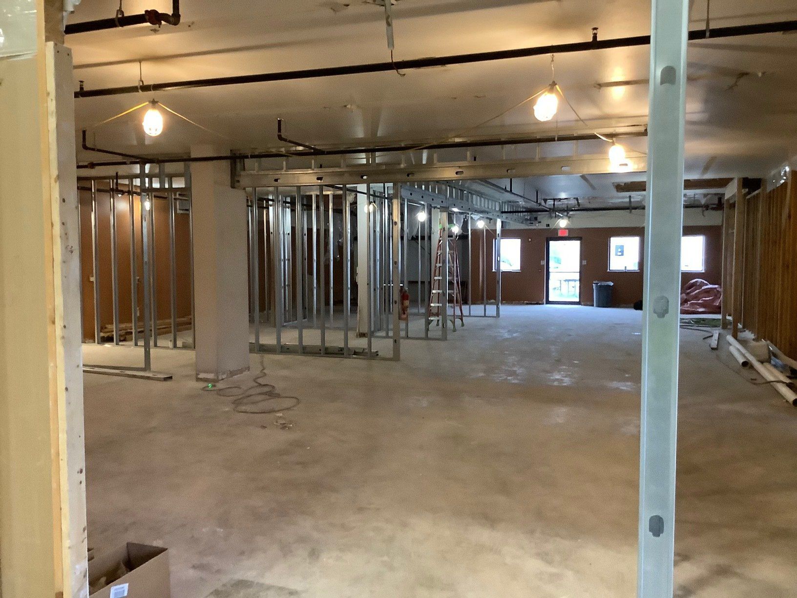 Interior view of a construction site with metal studs outlining future walls, exposed ceiling, and concrete floor.