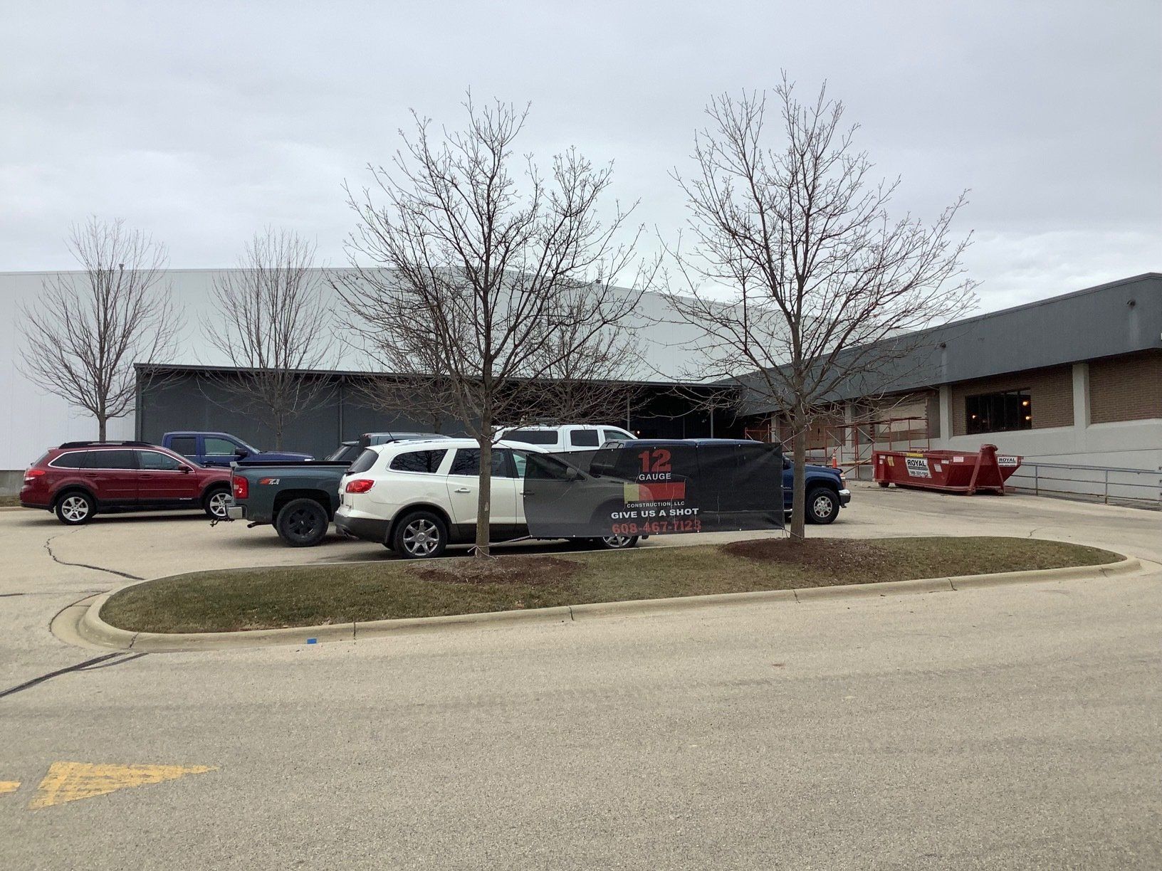 Cars parked outside a commercial building on an overcast day; trees in front.