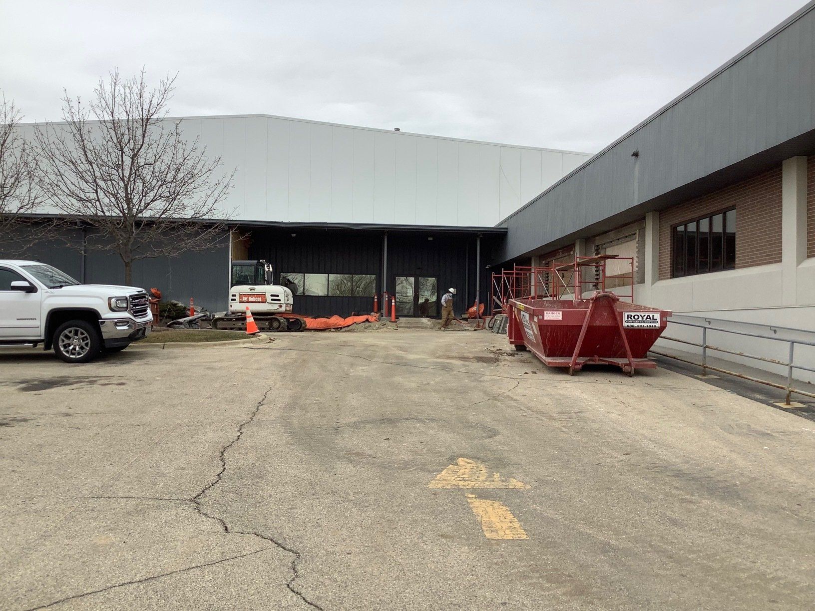 Construction site outside a building: a dump container, excavator, and truck are present.