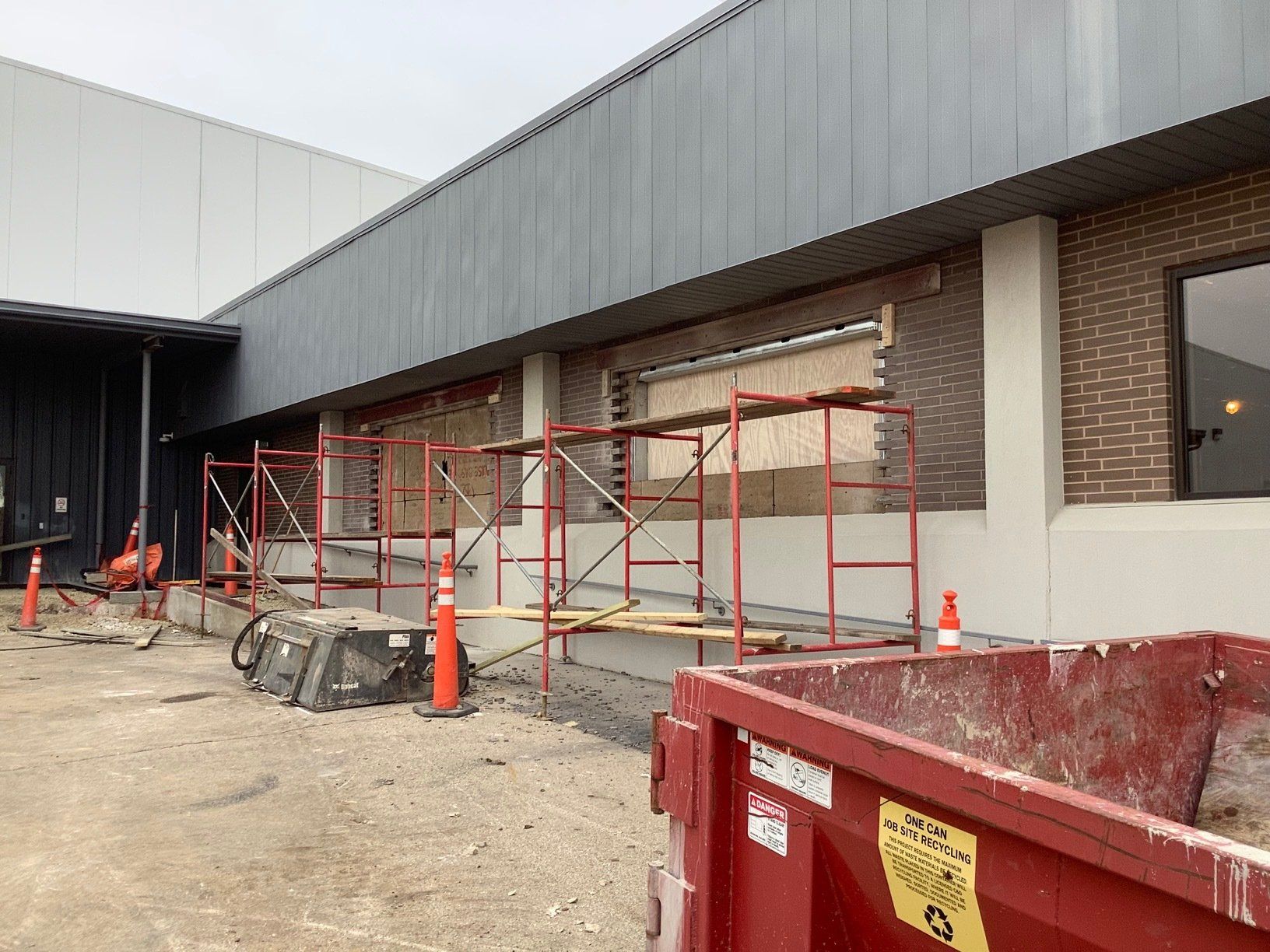 Construction site with scaffolding and red dumpster outside a building with brick and gray siding.