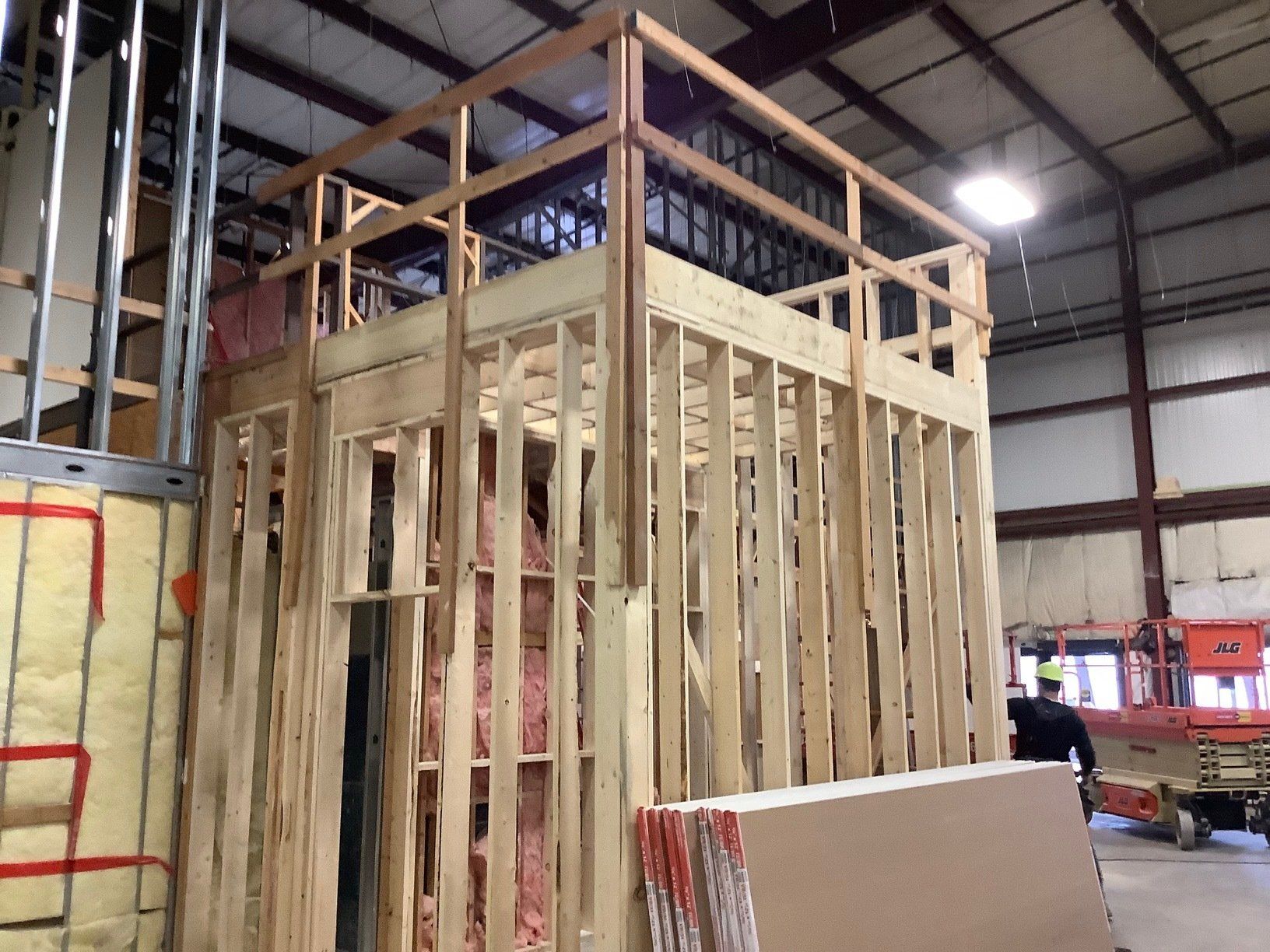 Wooden structure under construction, possibly a second story. Pink insulation visible. Person operating a lift.
