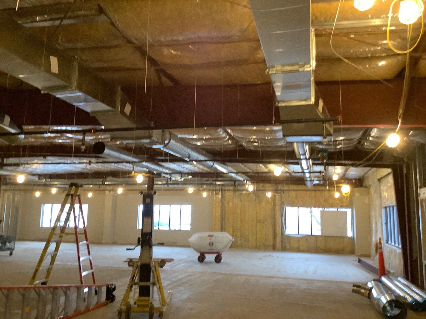 An unfinished interior space with exposed ductwork, windows, and construction equipment.