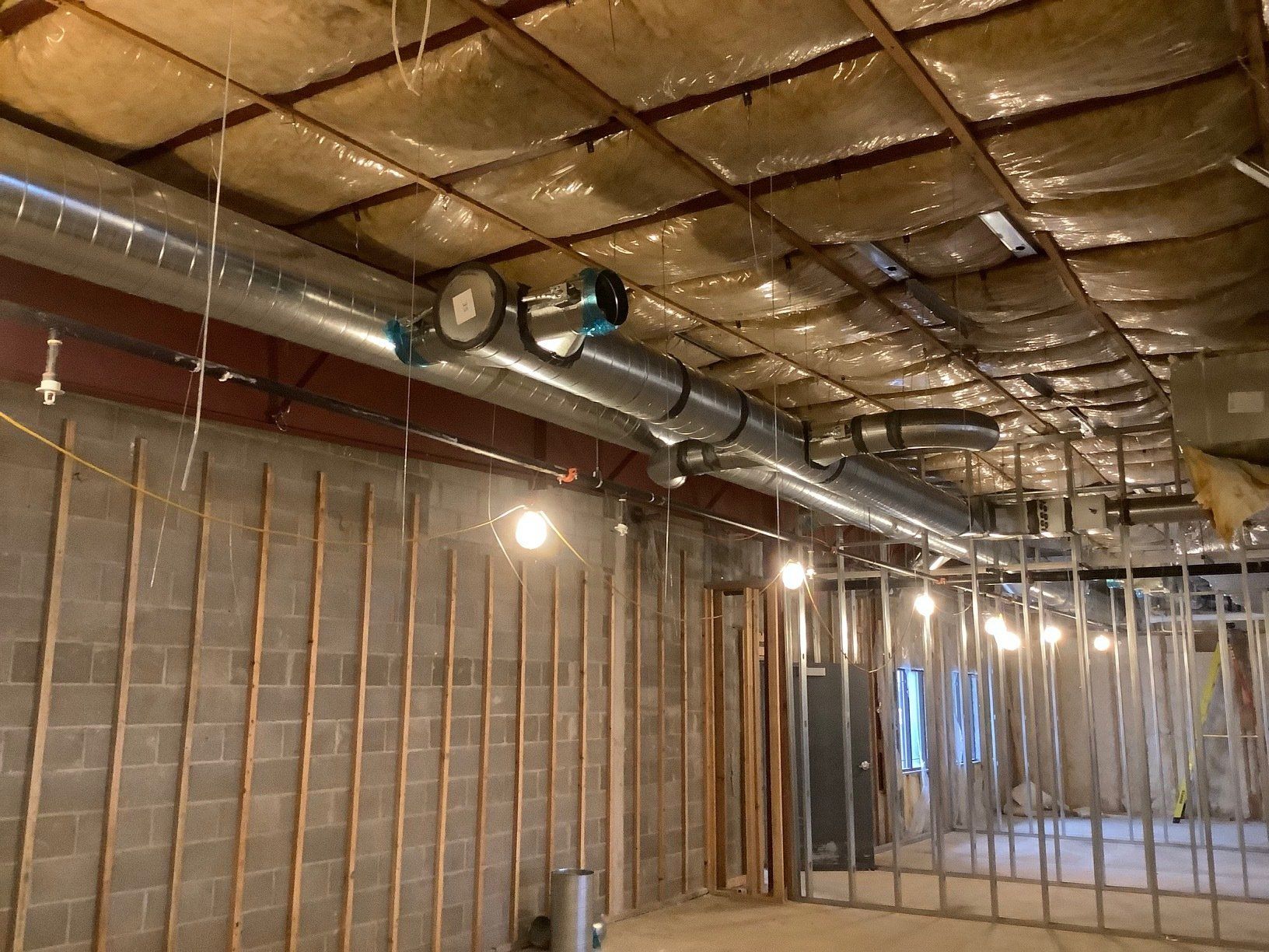 Interior under construction, showing ductwork, insulation, studs, and concrete block walls.
