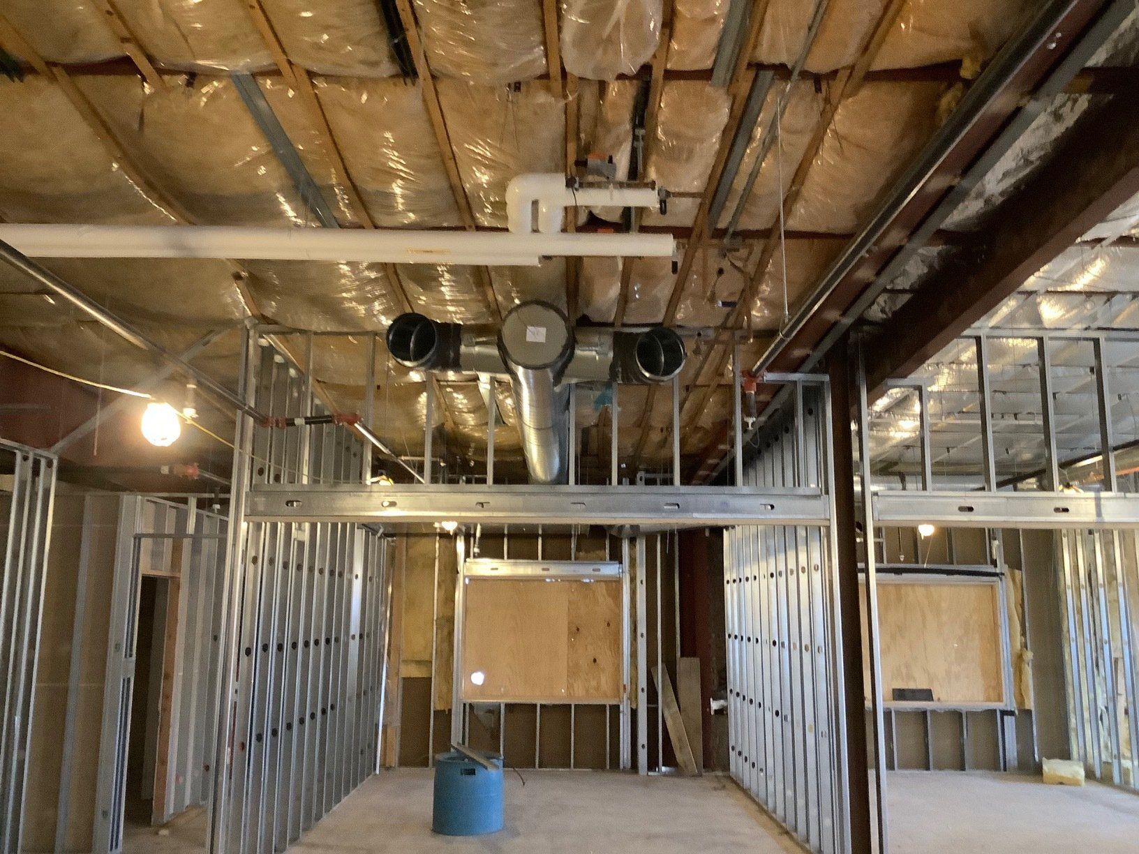 Interior construction scene: Metal framing, ductwork, insulation visible in a room under renovation.