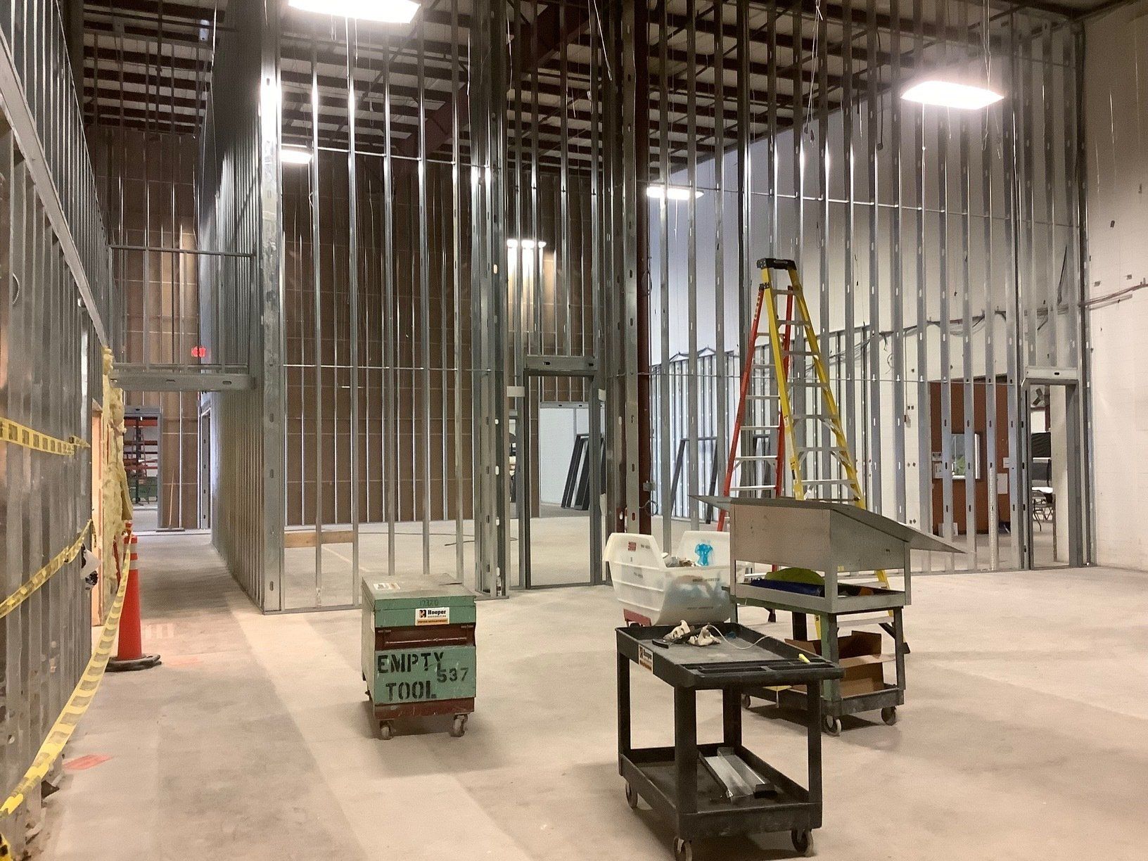 Interior of a building under construction, with metal studs framing walls and doorways. Construction equipment and materials are present.