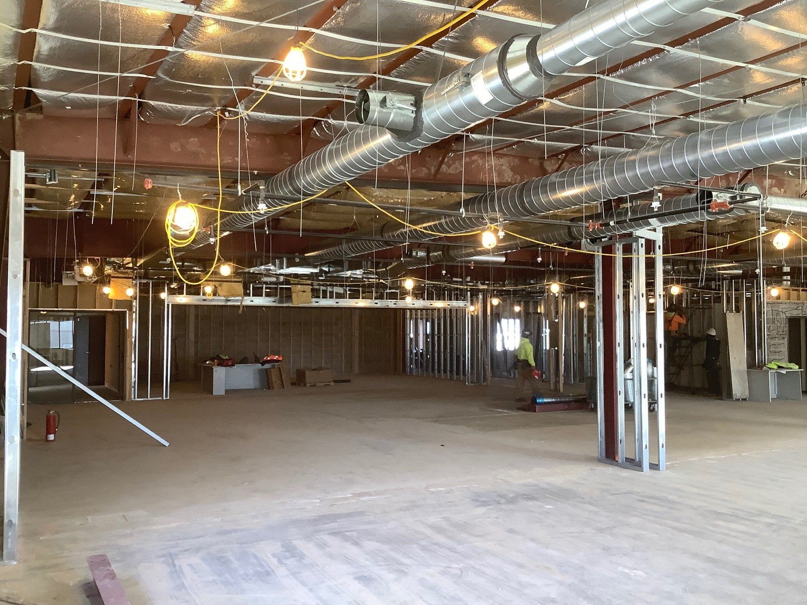 Interior construction site with metal framing, exposed ductwork, and overhead lighting.