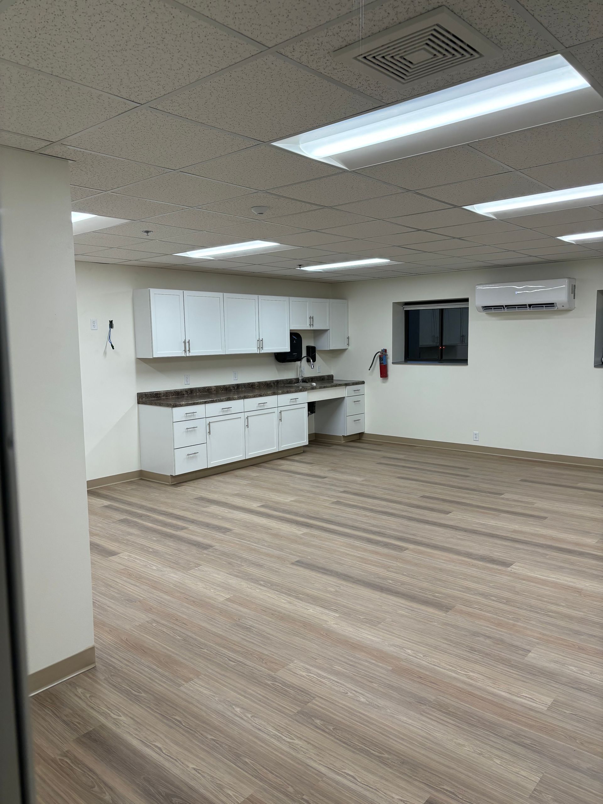 An empty room with wood-look flooring, white cabinets, and fluorescent lights in the ceiling.