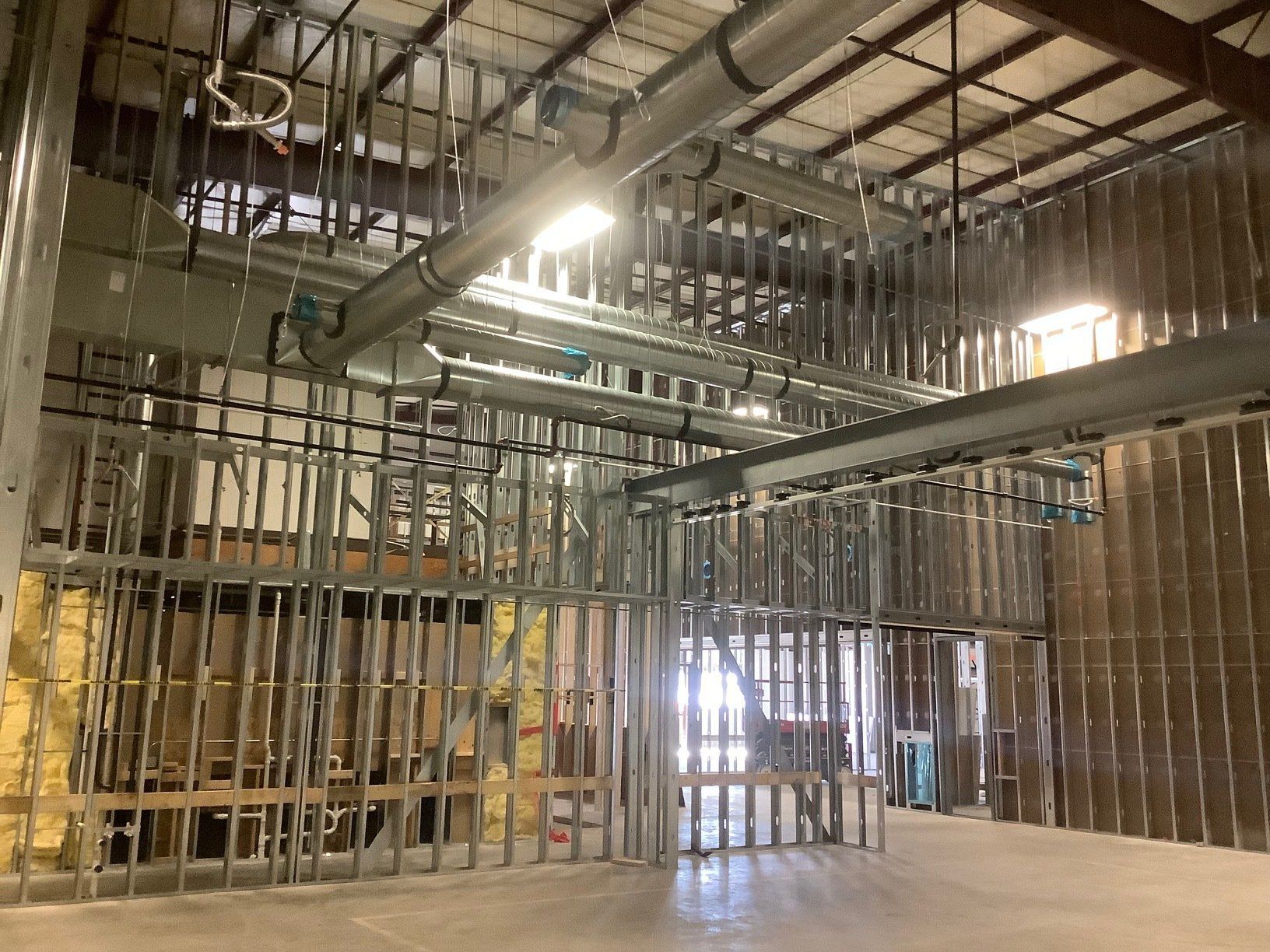 Interior of a commercial building under construction; metal studs, ductwork, and exposed insulation visible.