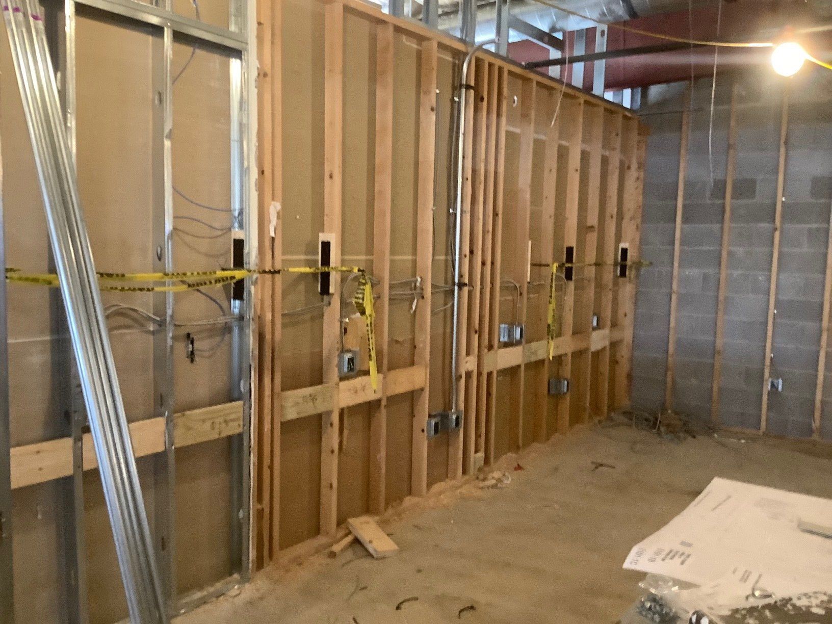 Construction site with exposed wall studs, electrical boxes, and wiring, concrete block wall, and unfinished floor.