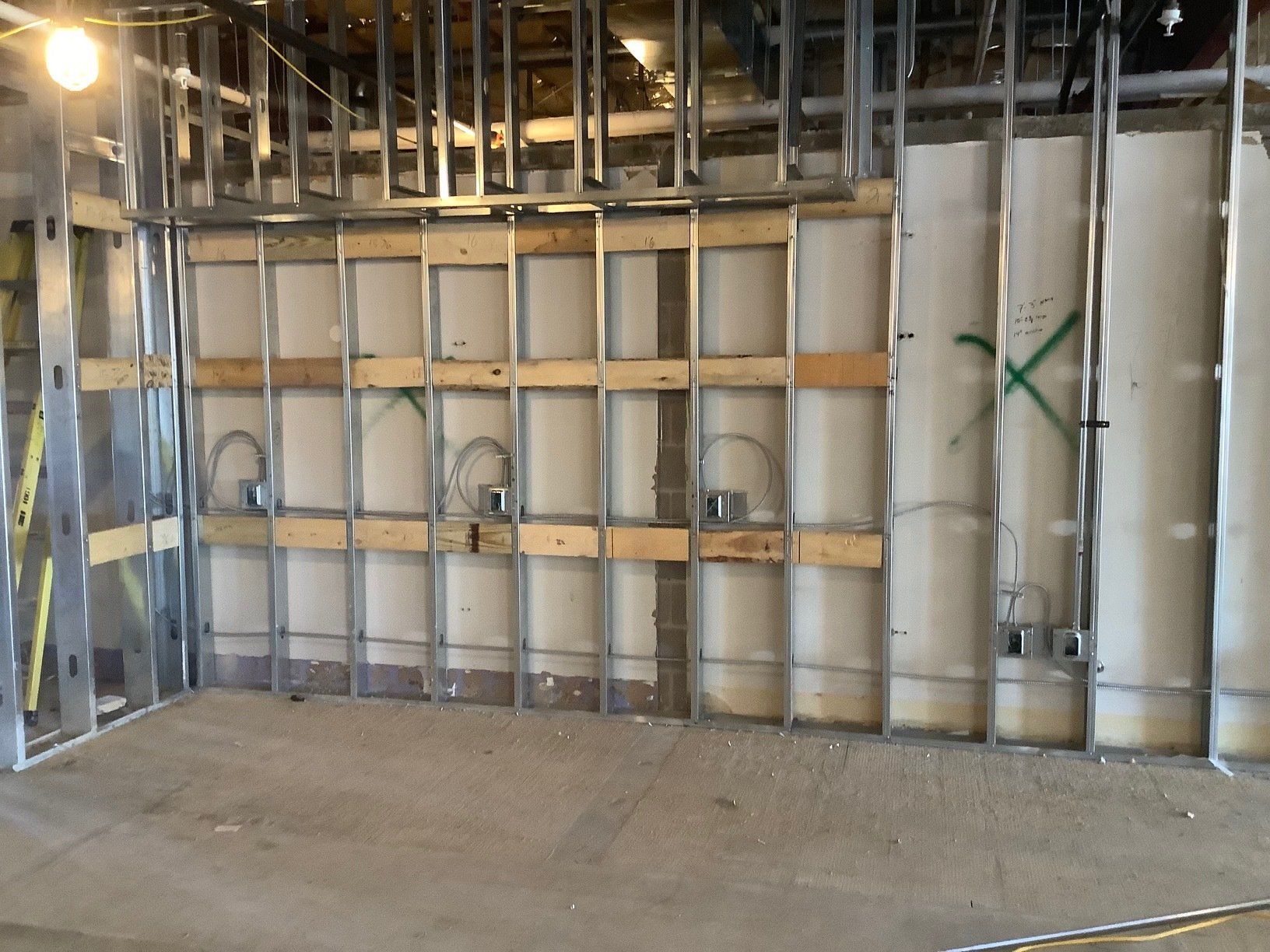 Metal framing for a wall interior, with electrical boxes and wiring visible, in a room under construction.