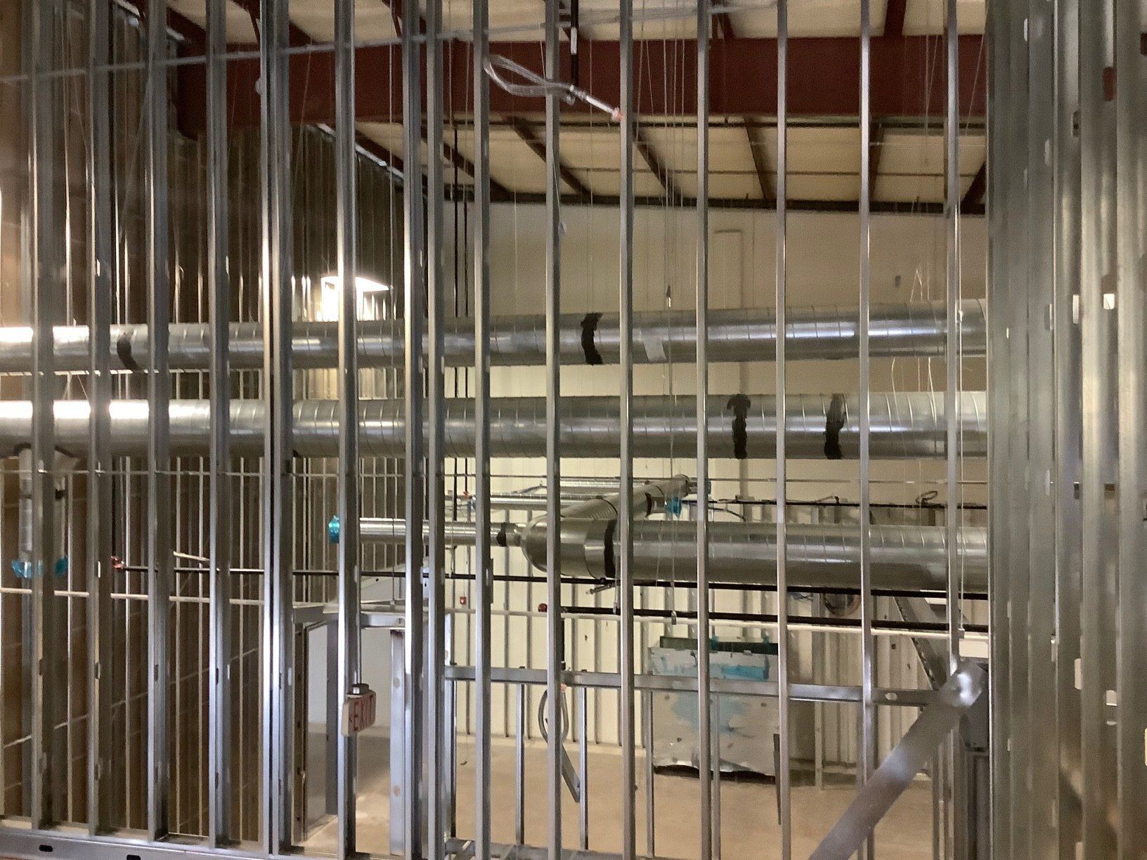 Metal studs frame a room with visible pipes and ductwork. Construction in progress.