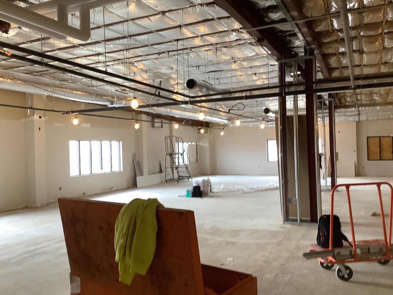Interior of a room under construction, with exposed pipes and insulation on the ceiling.