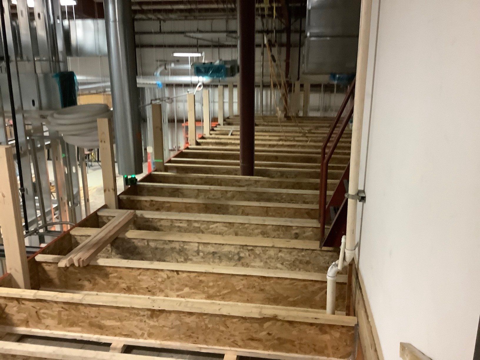Interior view of unfinished wooden stairs with supporting beams and a central pipe.