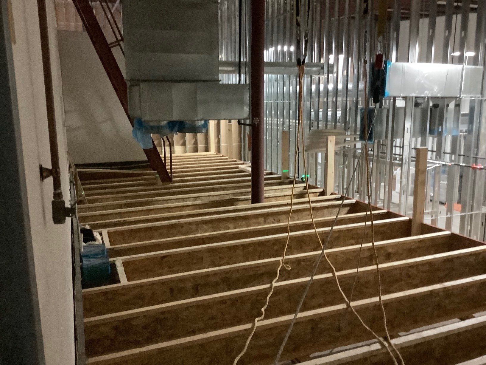 Construction site with exposed floor joists, metal studs, ductwork, and pipes.