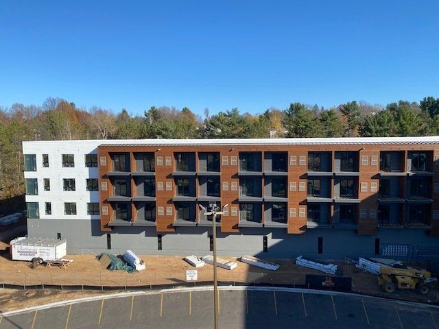 Multi-story apartment building under construction, featuring white and brown facades, blue sky background.