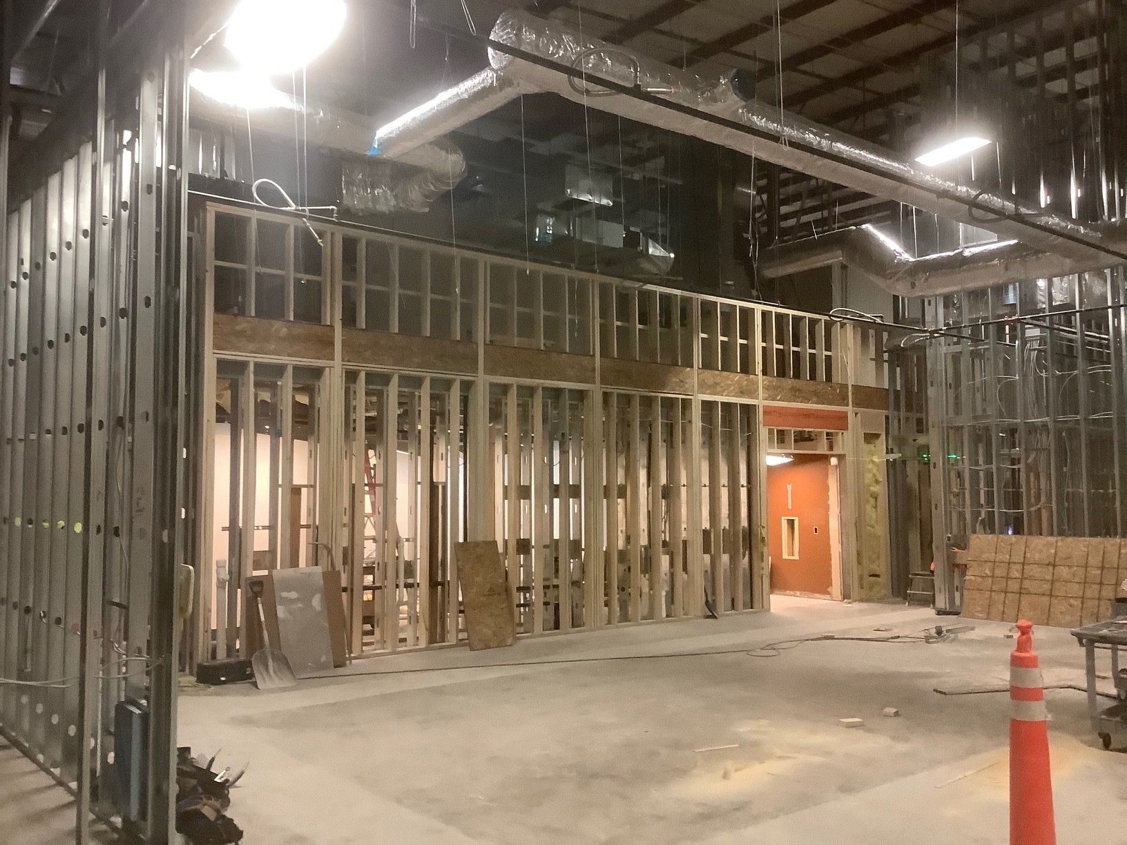 Interior view of a building under construction, with exposed framing, ductwork, and concrete floor.