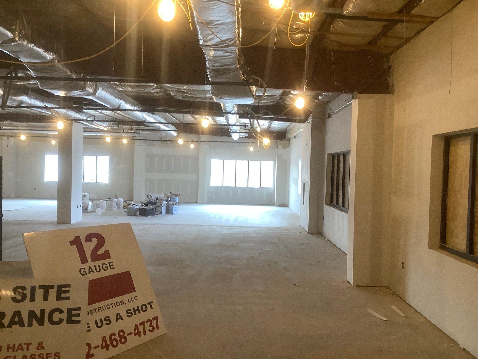 Interior of a construction site with exposed pipes, bare walls, and strung lights. A sign reads 