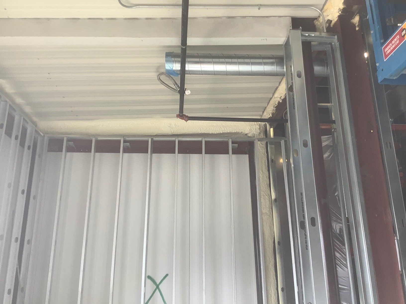 Metal framing with white corrugated paneling, ceiling with ductwork, electrical wires.