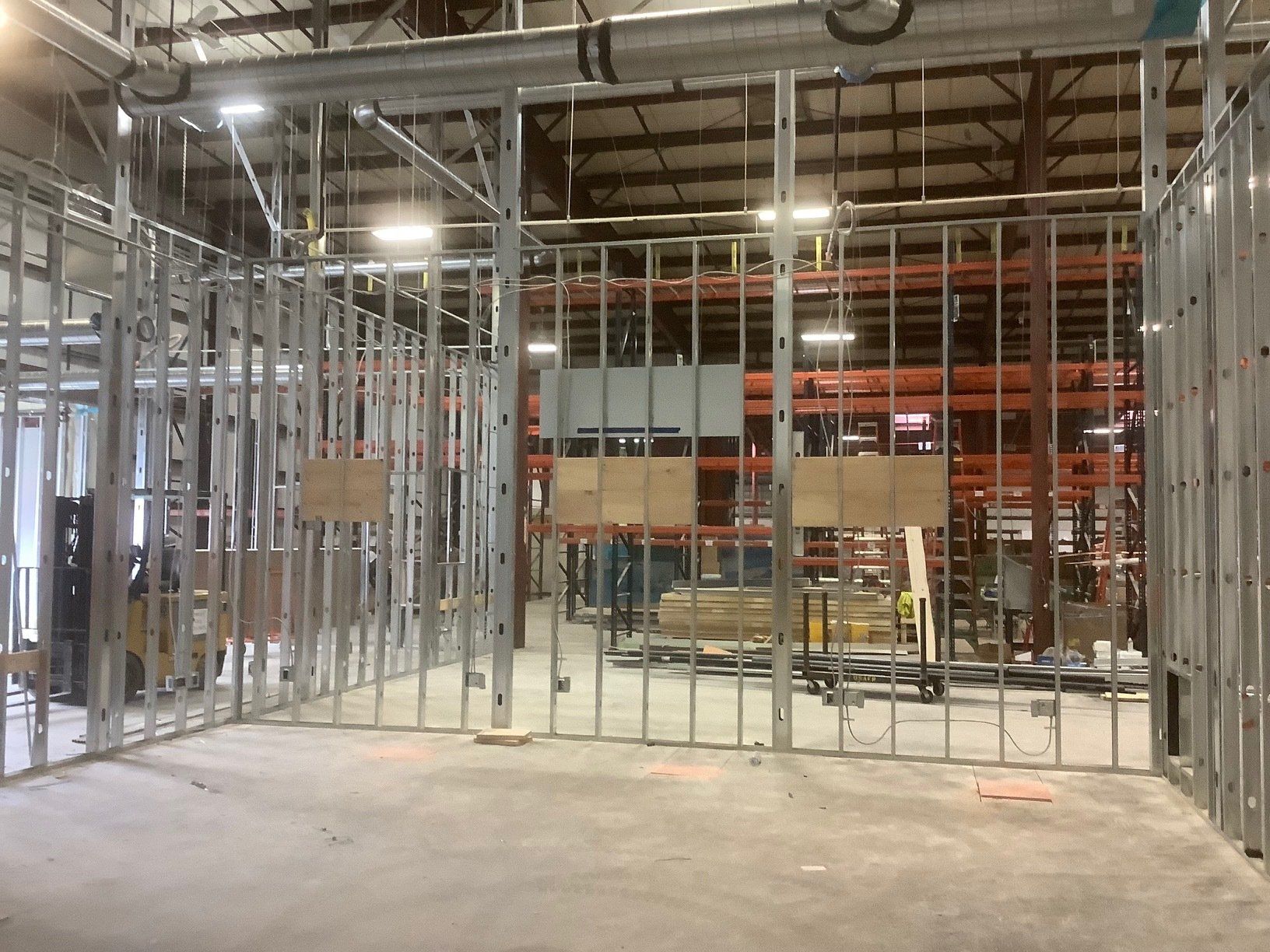 Metal frame walls under construction in a warehouse; gray concrete floor, exposed ceiling.