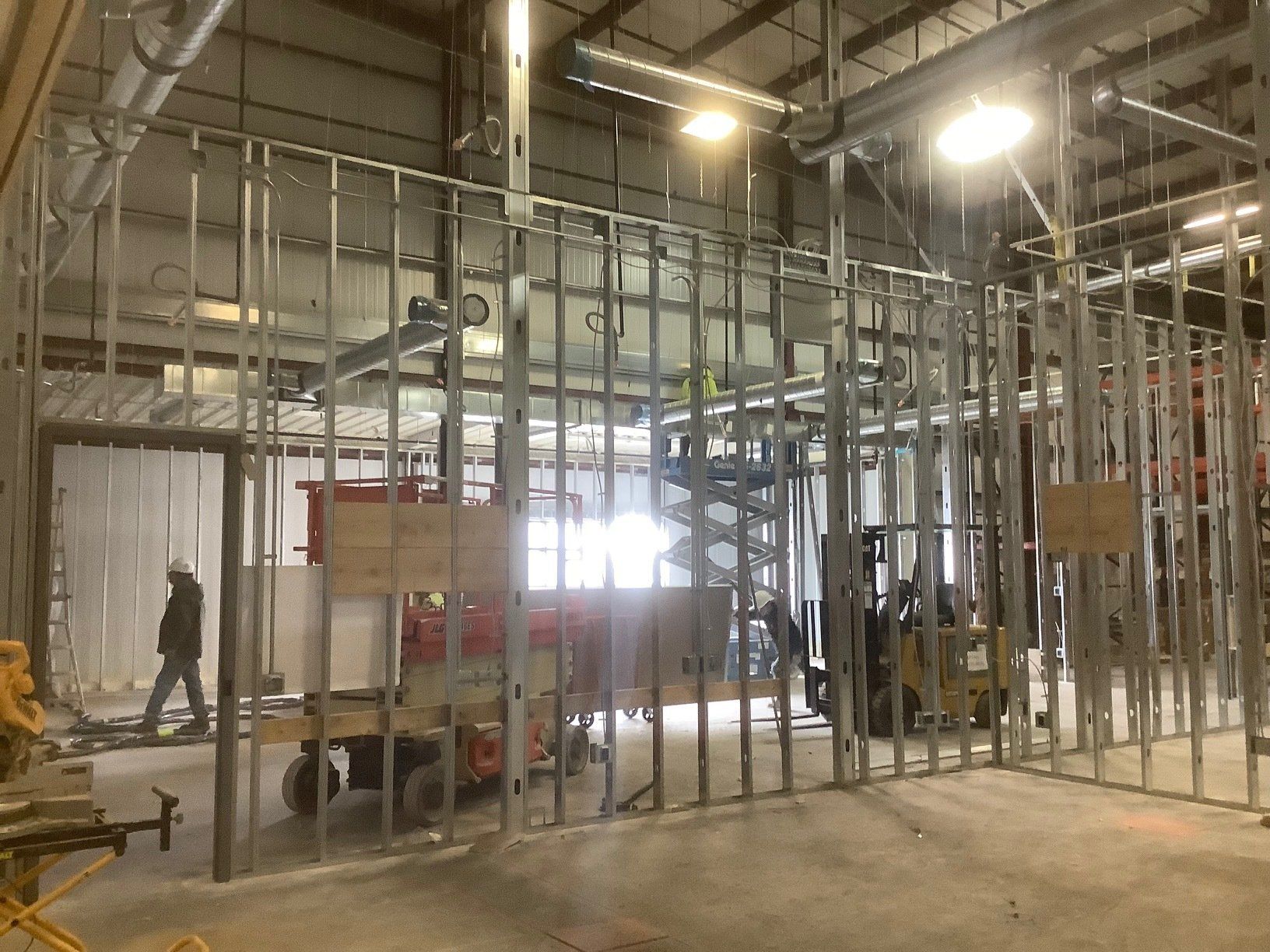 Interior view of metal stud framed walls under construction with a worker walking.