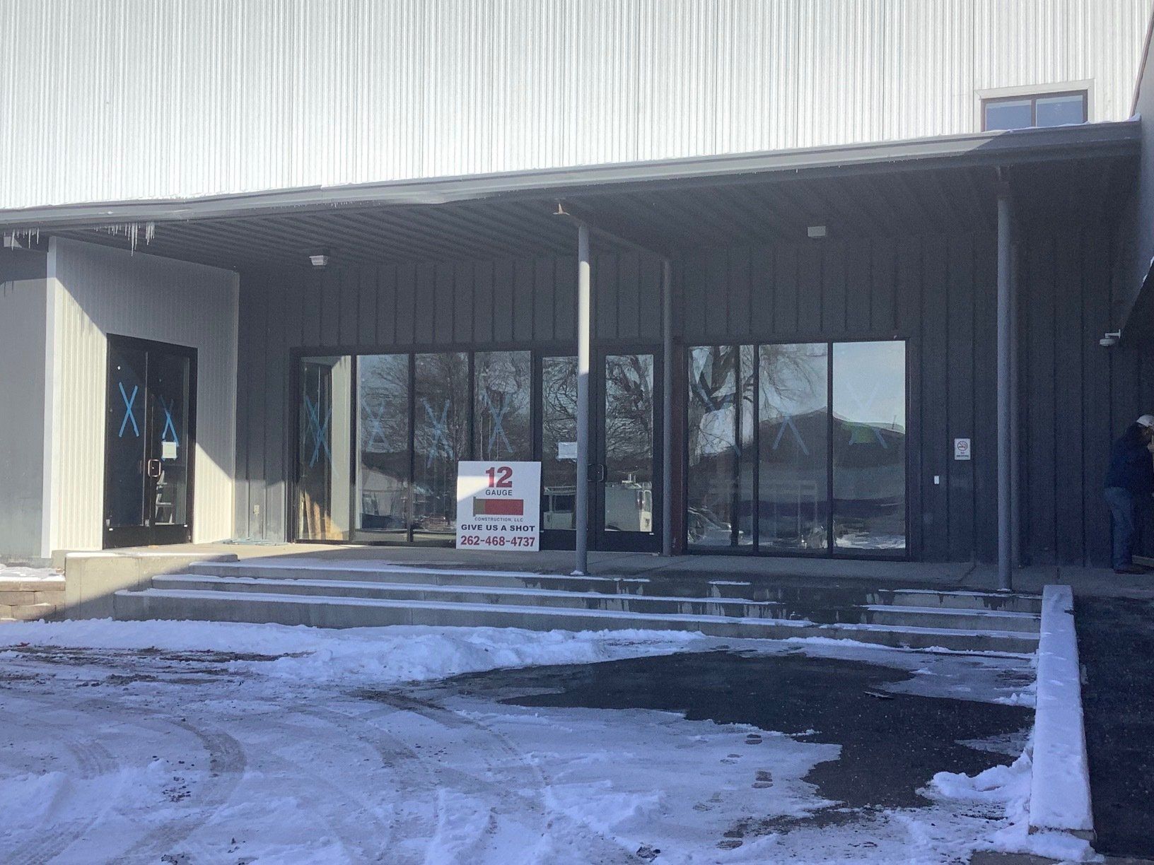 Exterior of a building with dark gray siding, large windows, and a covered entrance with snow on the ground.